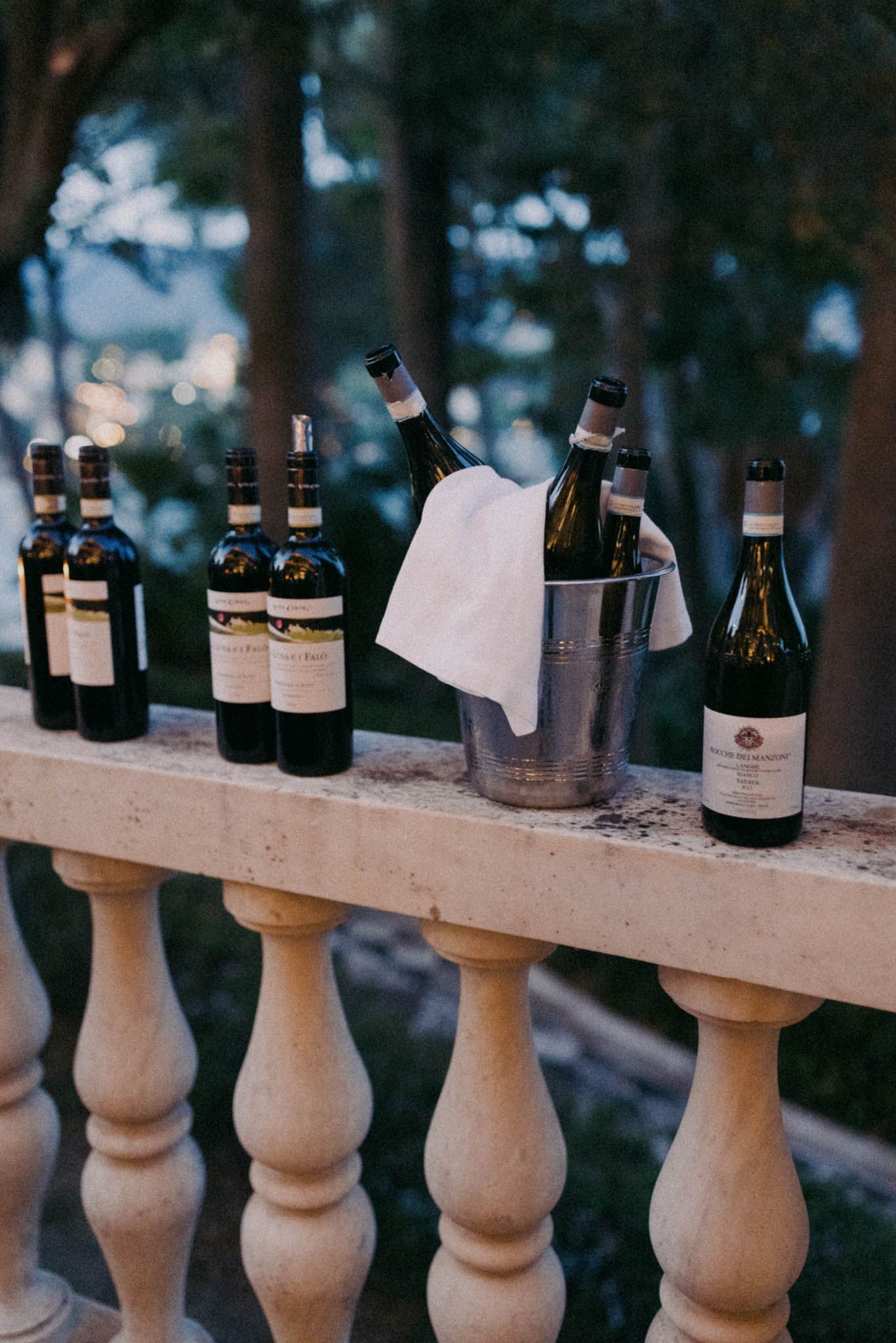 Empty glass bottles lined up on an outdoor stone balustrade railing at dusk.