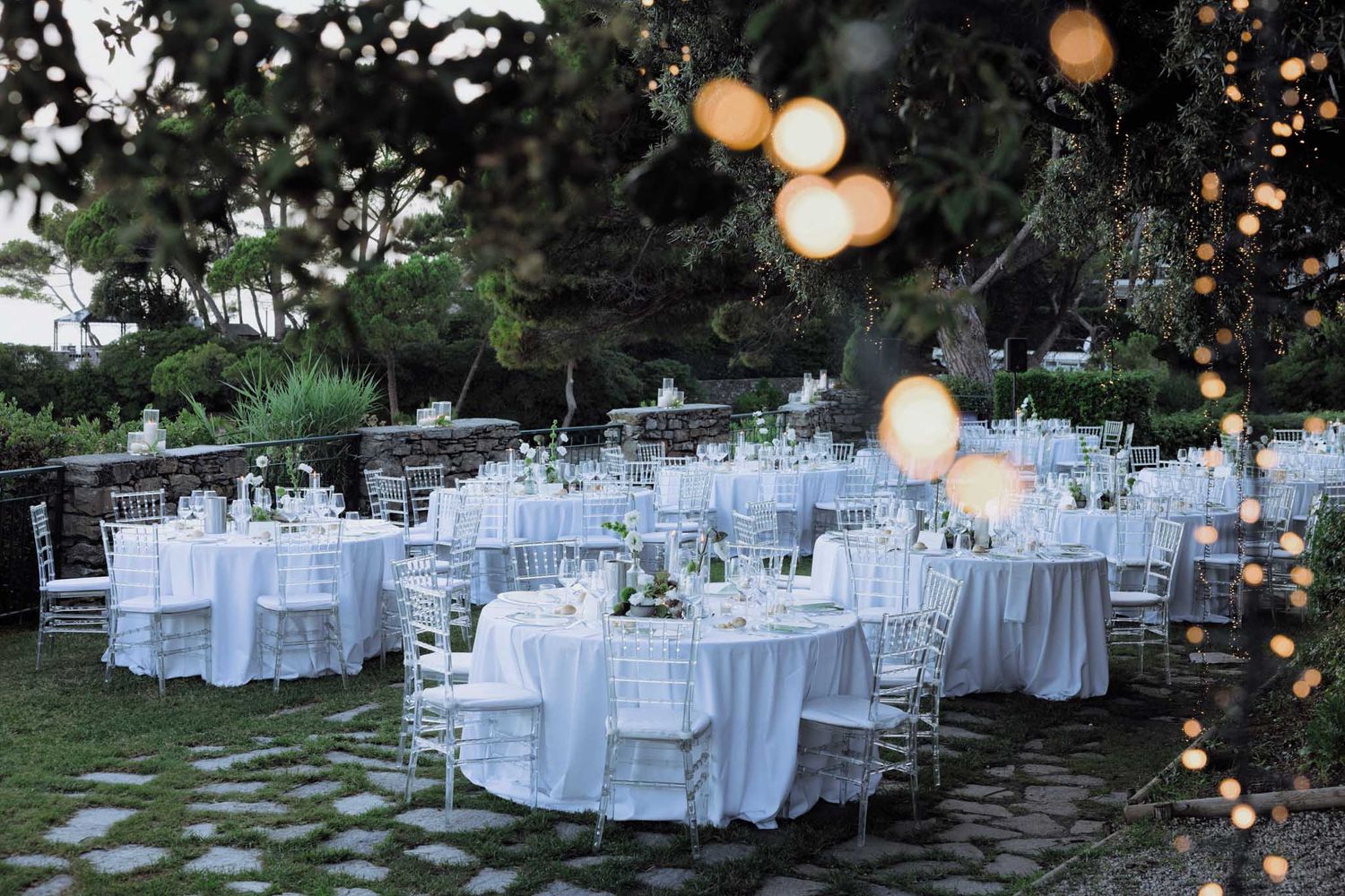 Elegant outdoor wedding reception setup with round white tables and string lights creating a romantic garden atmosphere.