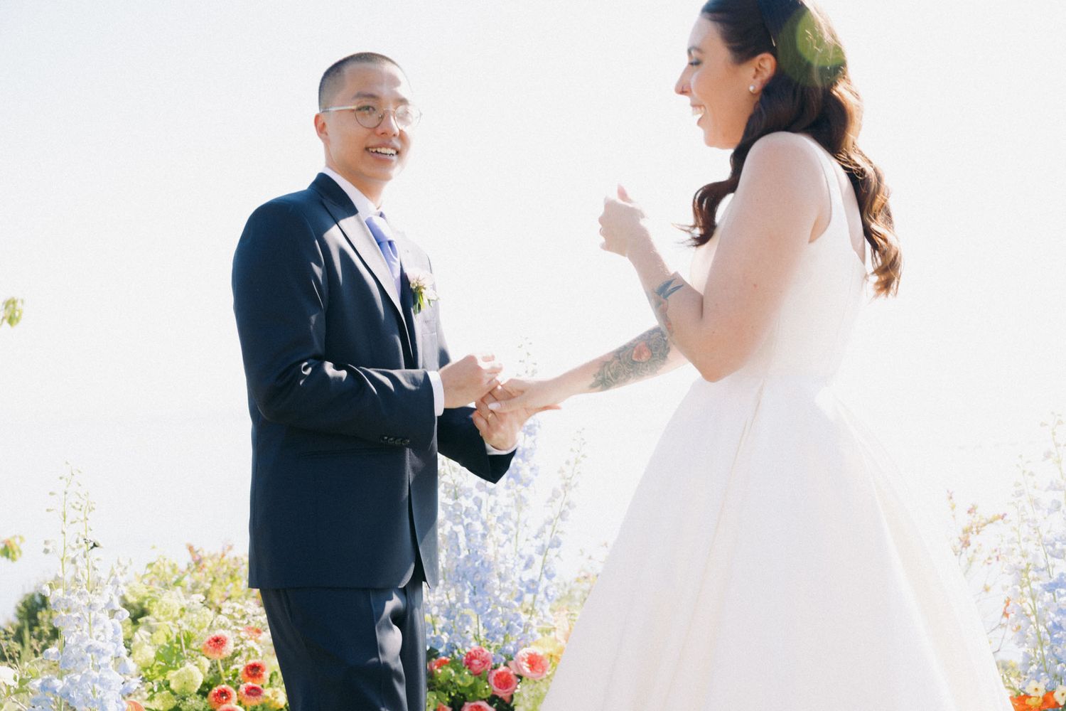 A couple shares a joyful moment during their outdoor wedding ceremony surrounded by colorful flowers.