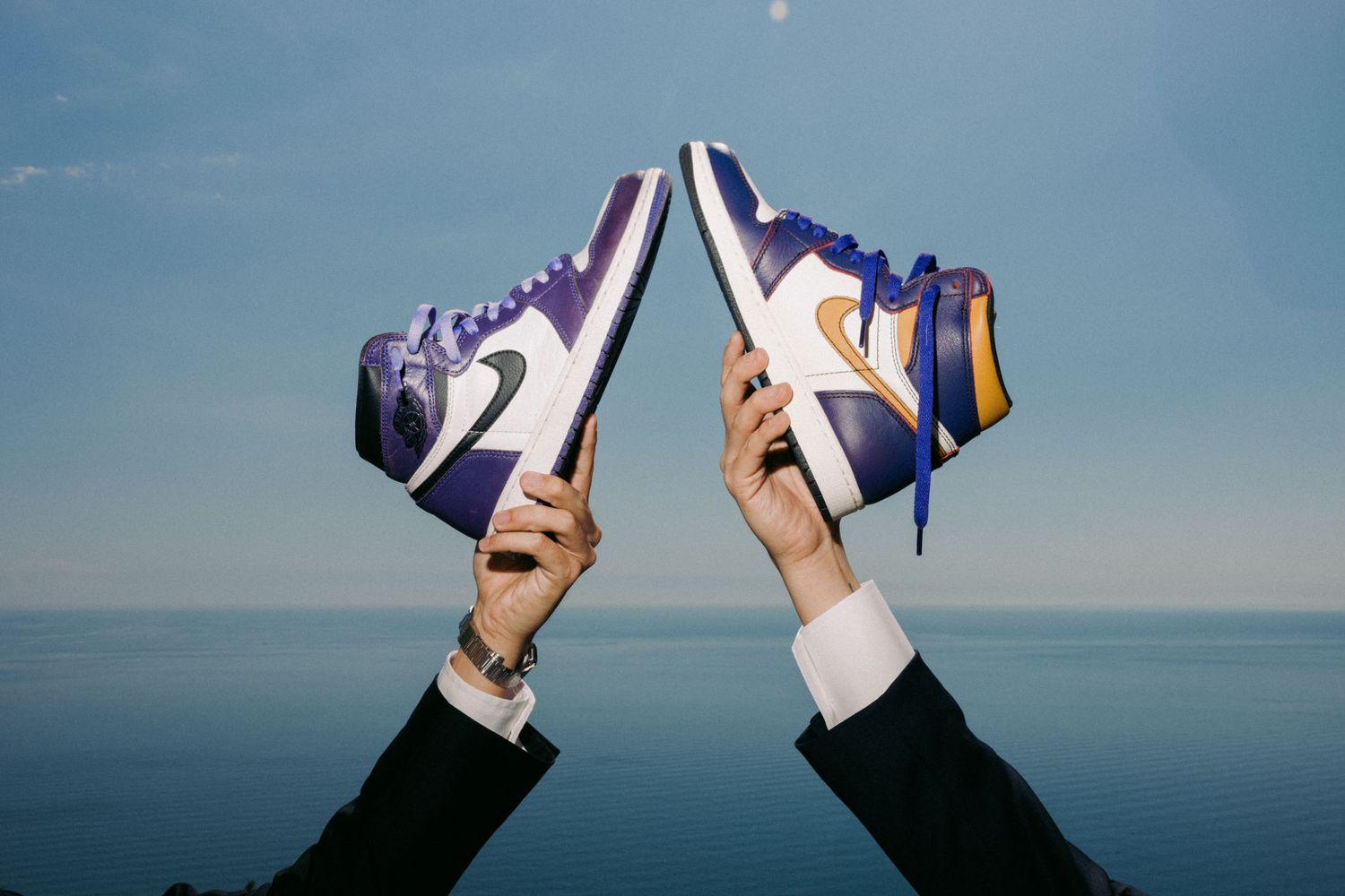 Multiple pairs of hands holding up sneakers against a blue sky background in a synchronized fashion.
