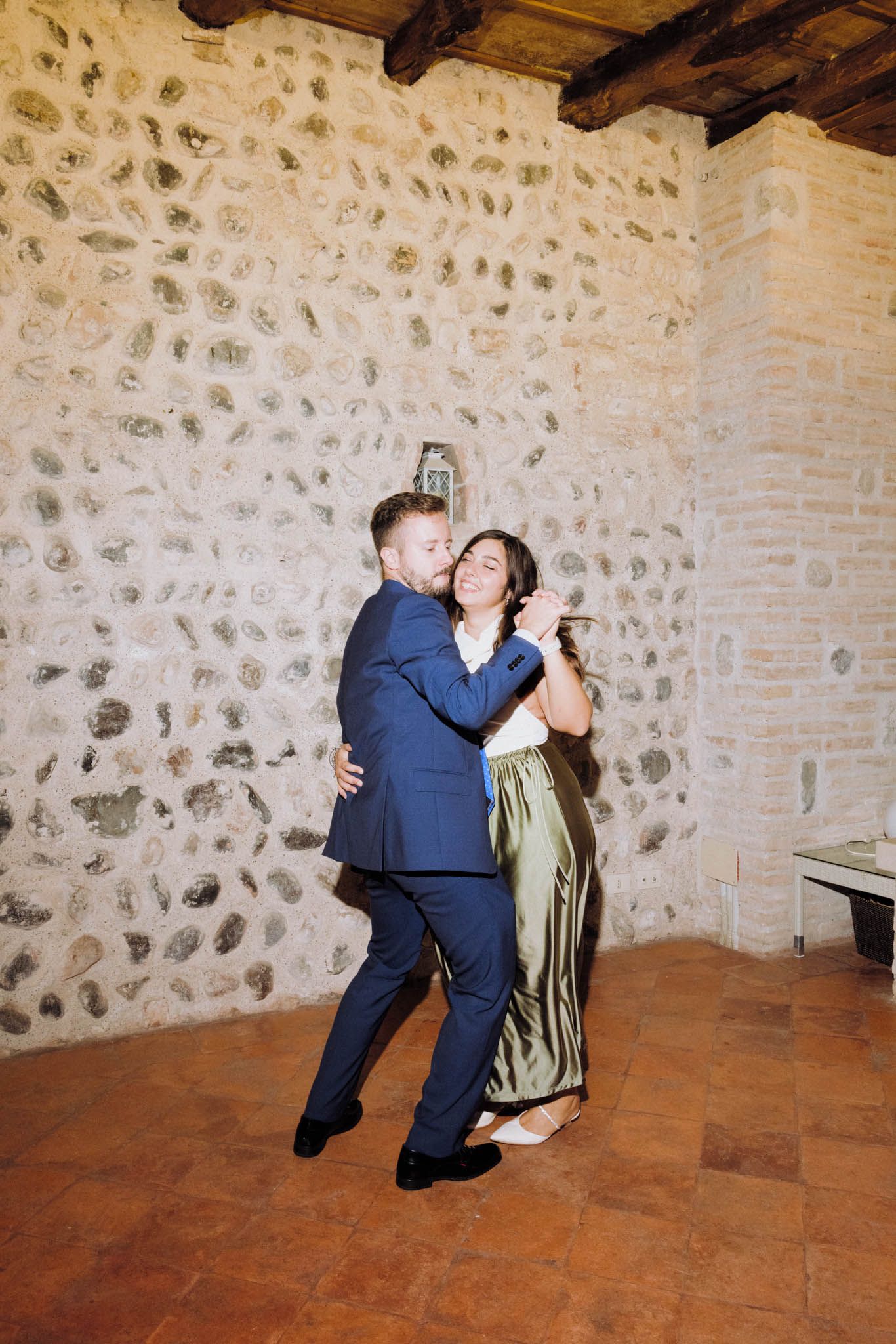 A couple dances together in a rustic stone-walled room with terracotta flooring.