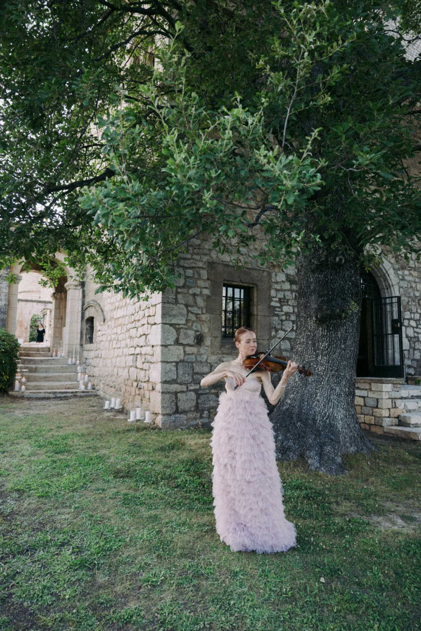 A person in a lavender tulle gown poses gracefully in a series of shots against a rustic stone wall and trees.