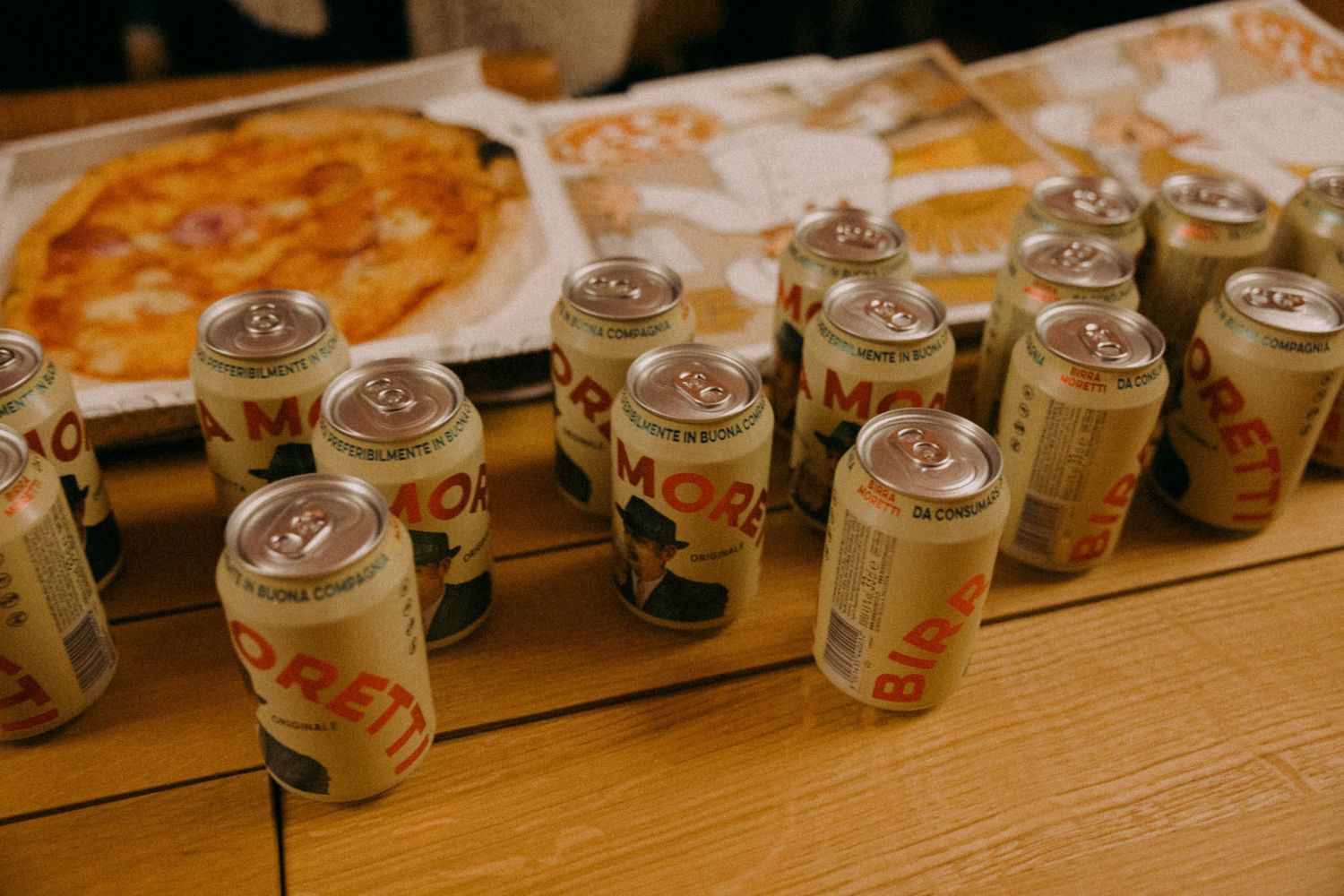 Row of empty Coors Light beer cans lined up on a wooden surface next to pizza slices.