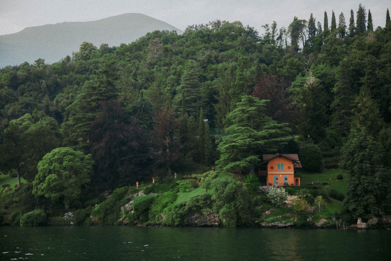 Scenic view of Lake Como with lush green mountains and cypress trees along the shoreline.