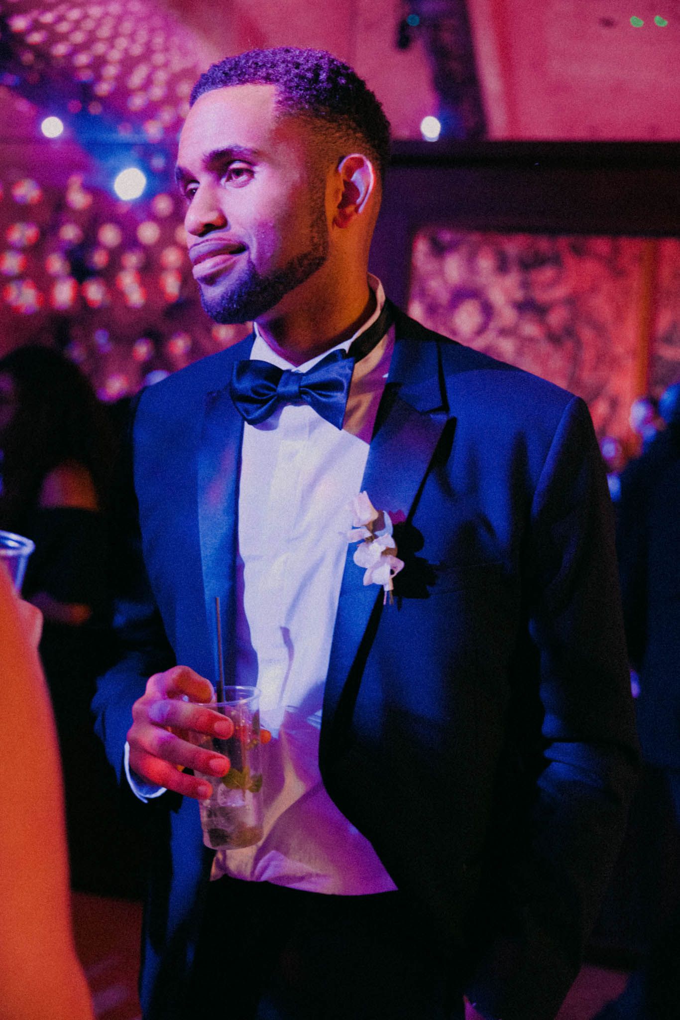 A person in a tuxedo and bowtie enjoying themselves at a formal event under pink lighting.