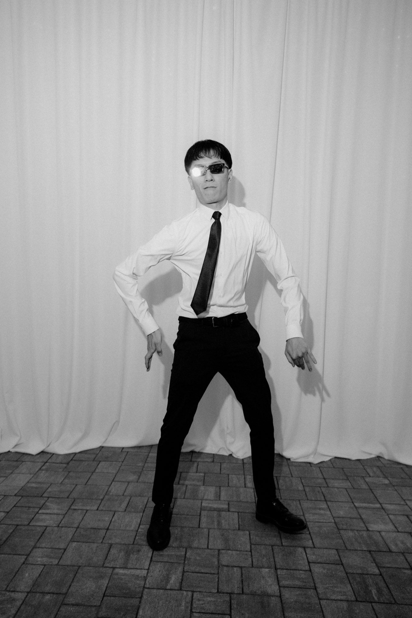 A sequence of black and white photos showing a person in formal attire performing dynamic dance movements against a wall.