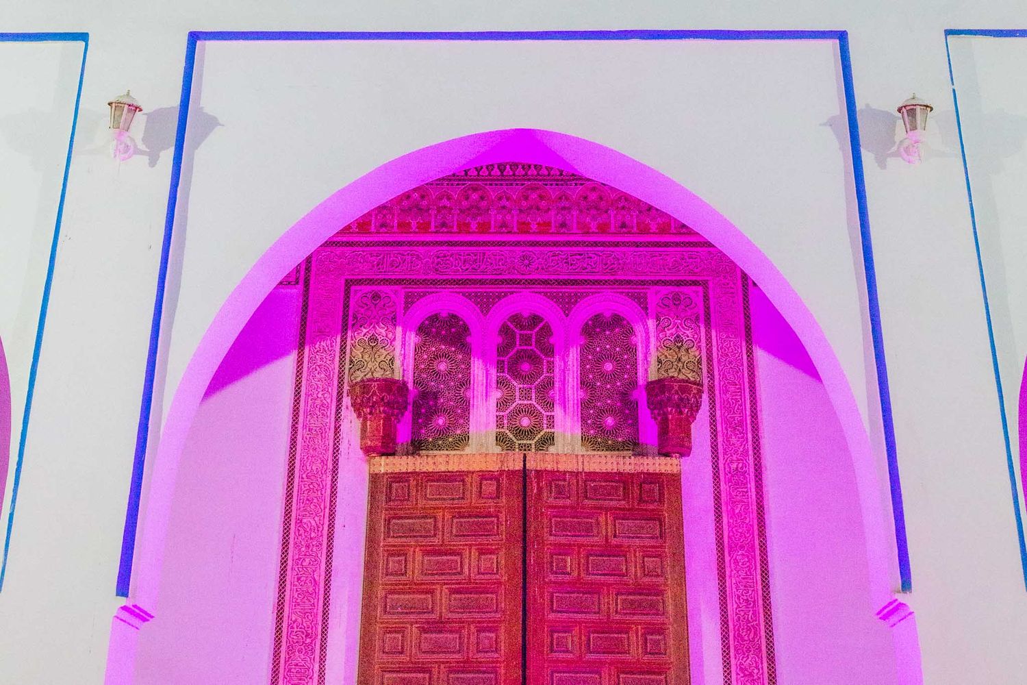 Ornate pink-lit Moroccan doorway with traditional geometric patterns and arched architectural details.