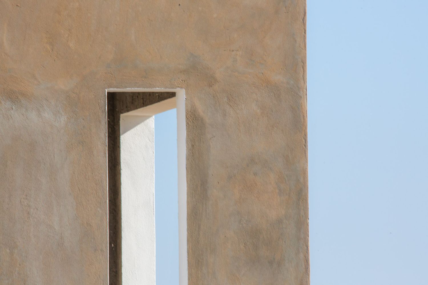 Abstract architectural detail showing beige walls with vertical window openings against a bright sky.