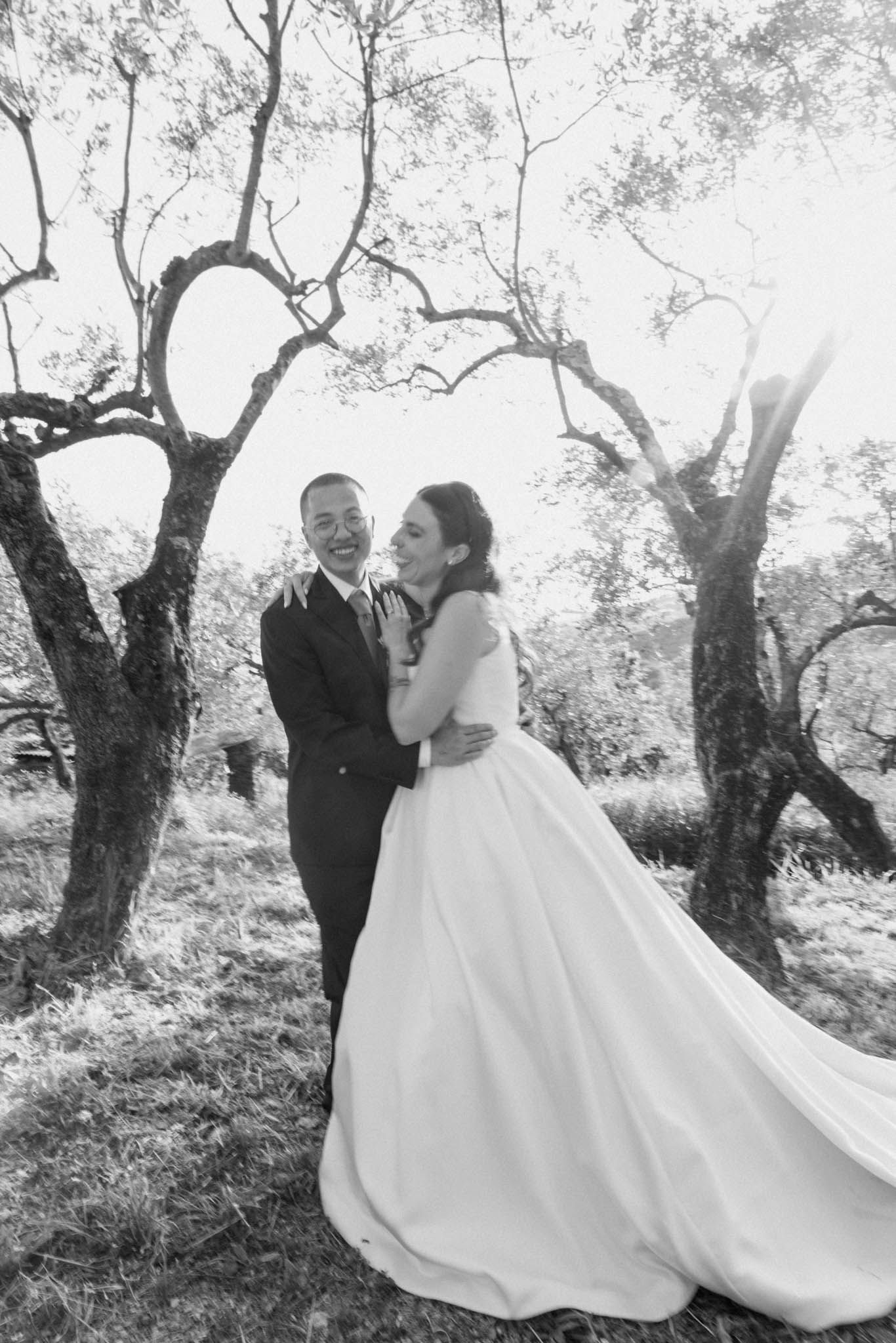 A romantic black and white wedding photo series showing a flowing white dress against a backdrop of olive trees.