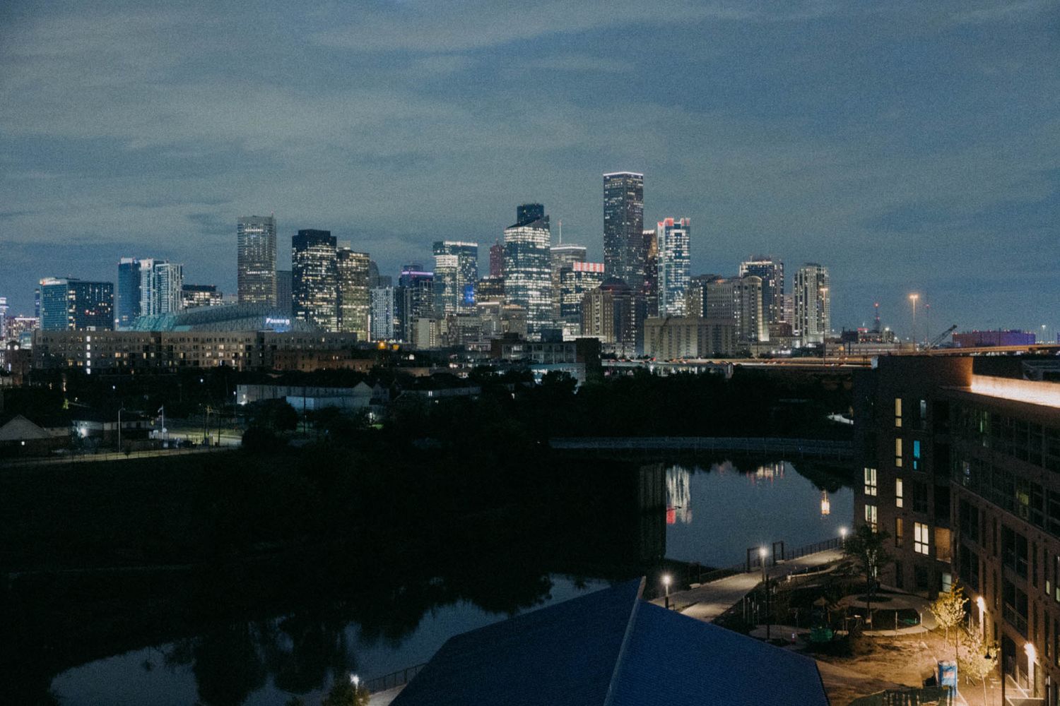 Panoramic cityscape of Boston skyline at dusk with illuminated buildings reflecting on the Charles River.