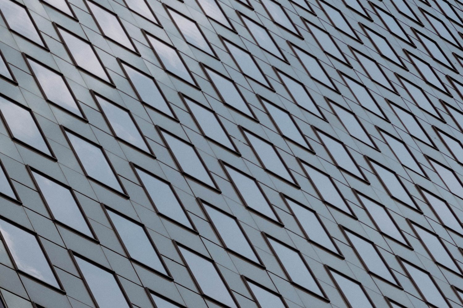 Abstract geometric pattern of diamond-shaped windows on modern building facade creating diagonal lines in gray tones.