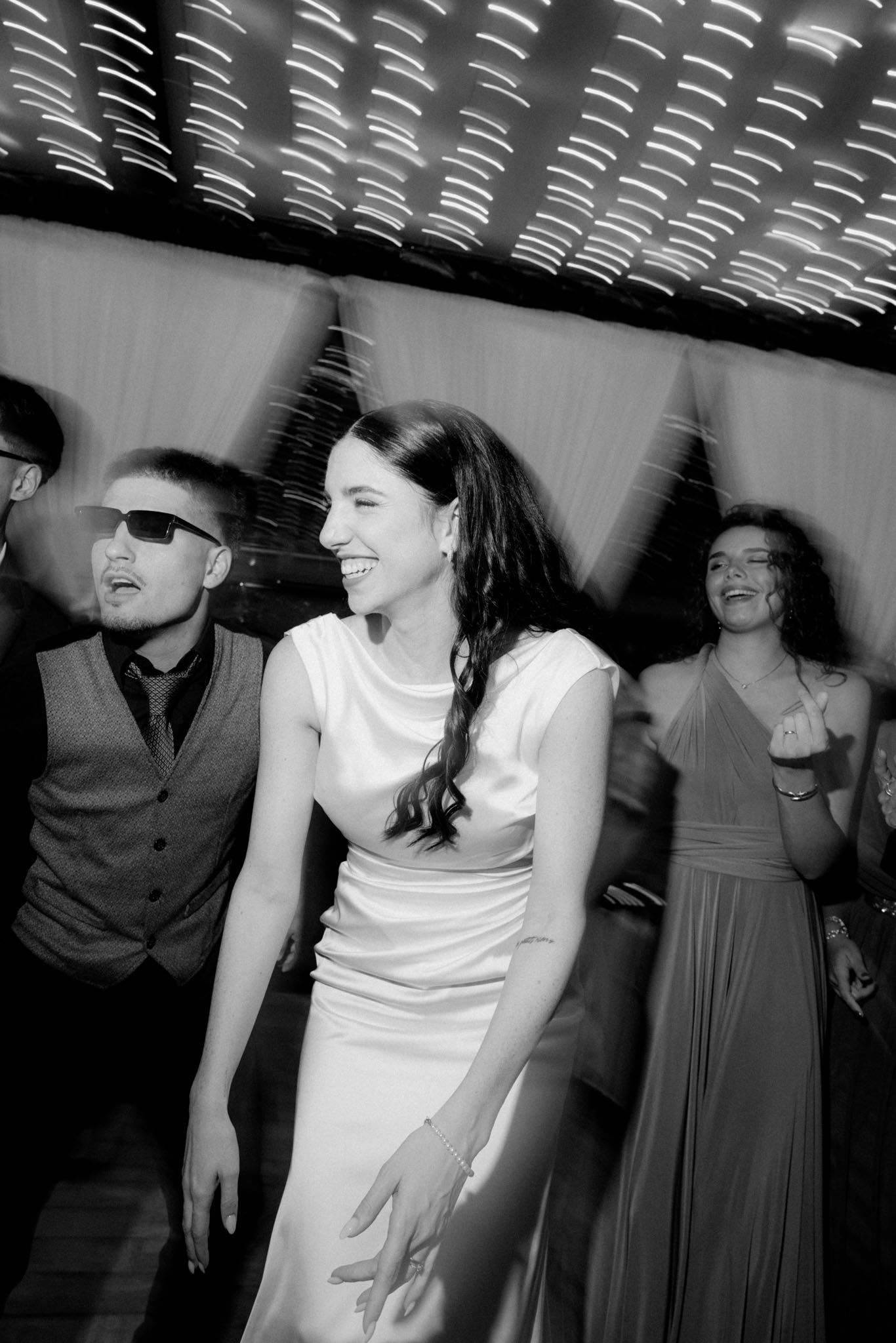 Black and white photo of people dancing at a party with disco lighting effects.
