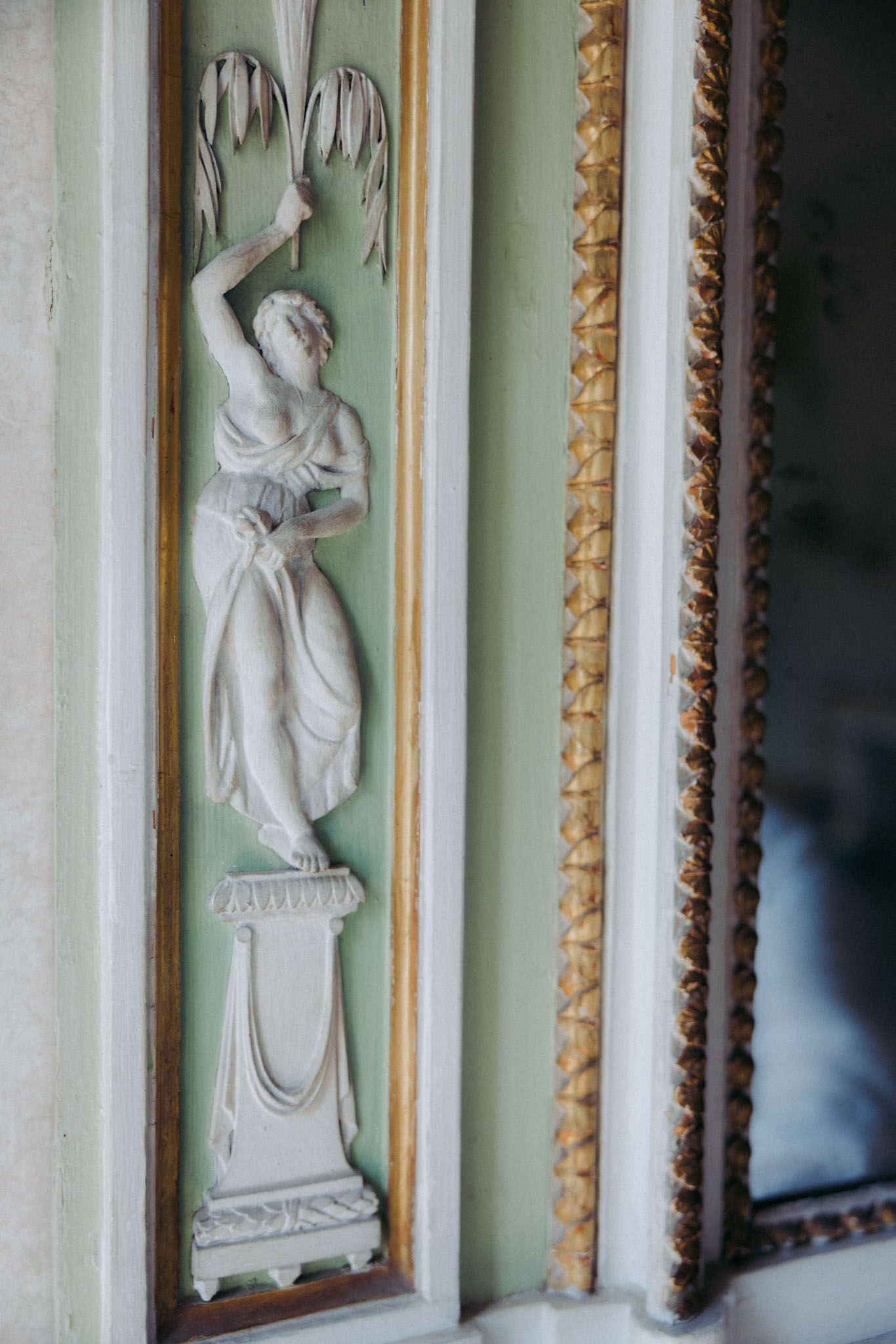 Ornate white neoclassical wall reliefs with decorative gold trim frames against a pale mint green background.