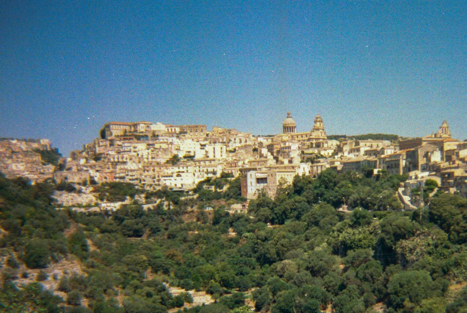 Panoramic view of an Italian hillside town with historic buildings and architecture against blue sky.