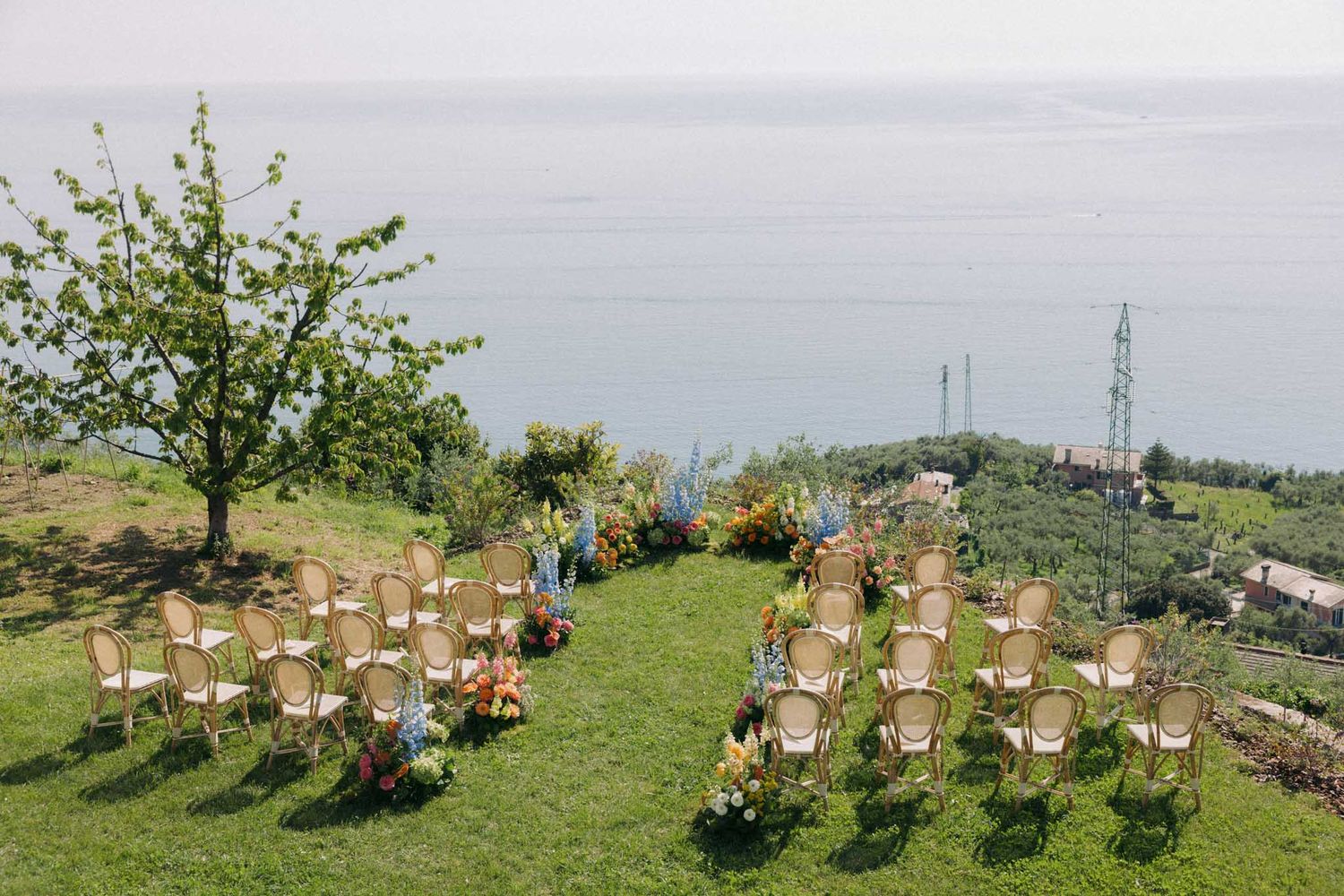 Wooden chairs arranged in rows on a grassy hilltop overlooking a scenic landscape on a sunny day.