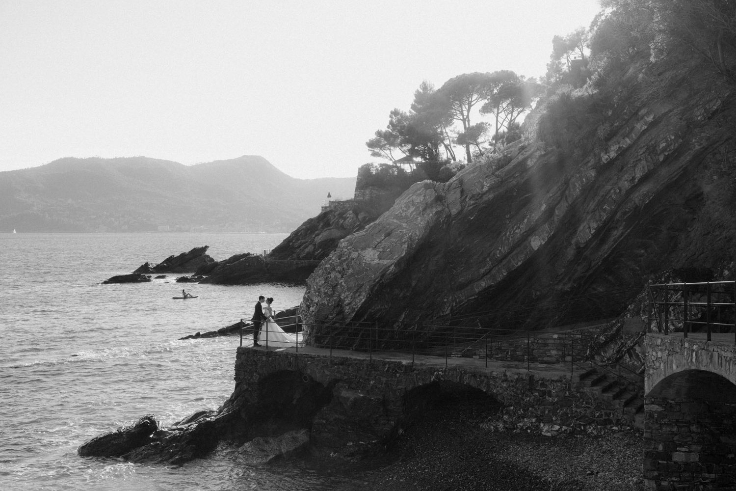 A dramatic black and white coastal landscape shows rocky cliffs meeting the ocean along a rugged shoreline.