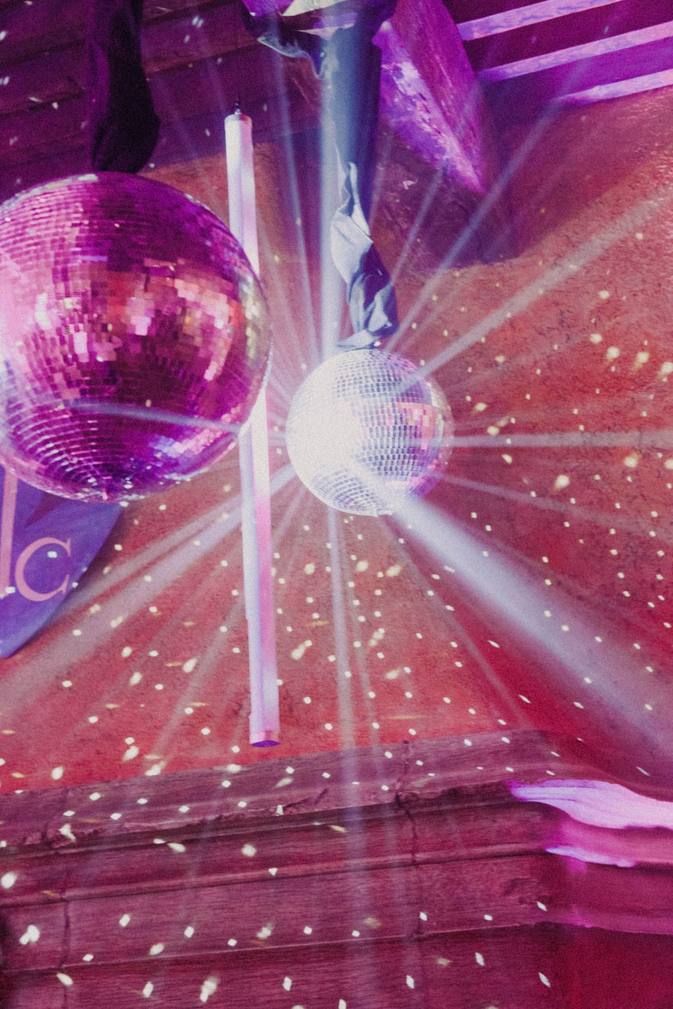 Mirrored disco ball reflecting sparkles and beams of light in a purple-lit dance club setting.