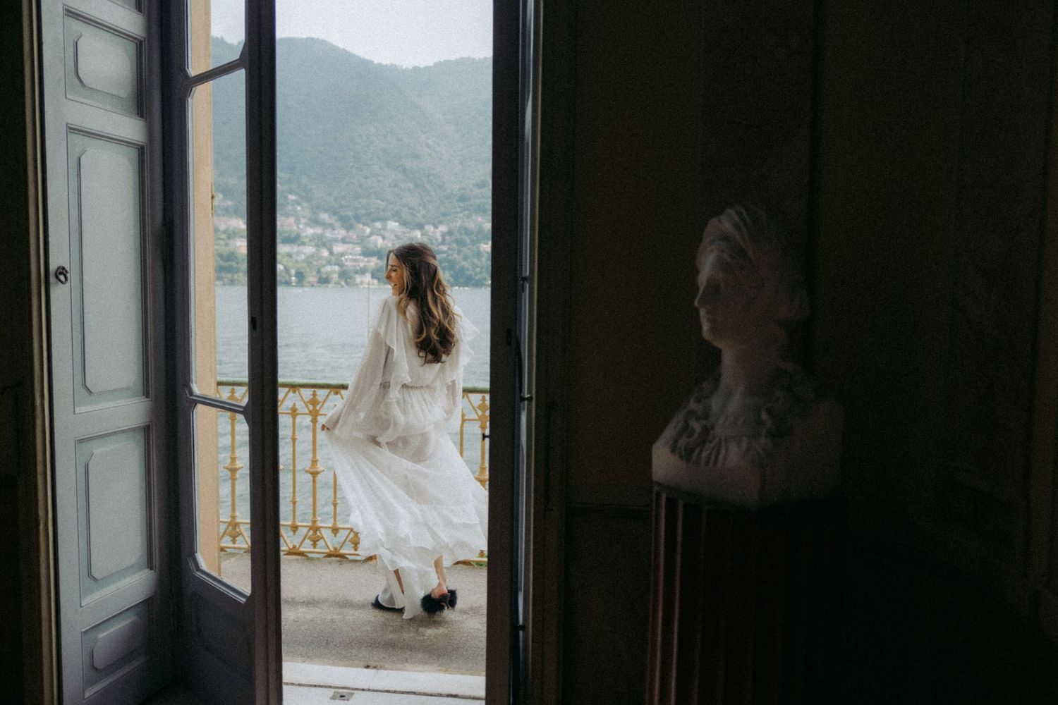A person stands in a doorway overlooking a misty mountain landscape with white curtains billowing in the breeze.