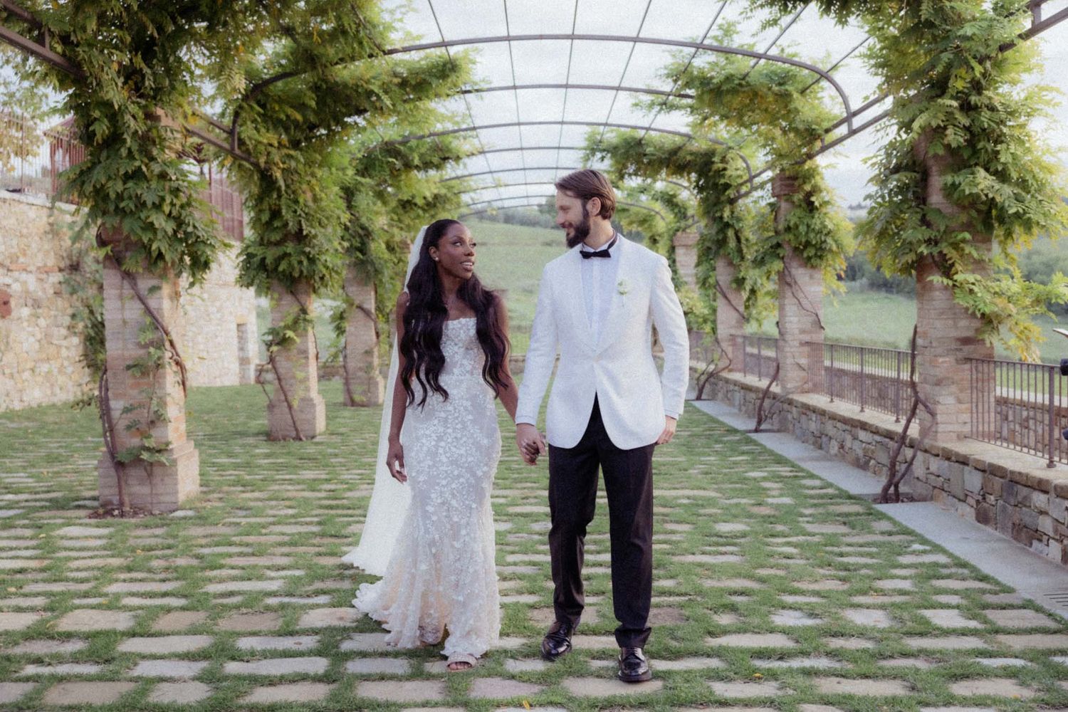 Couple walking hand in hand through a garden walkway covered with a translucent canopy.