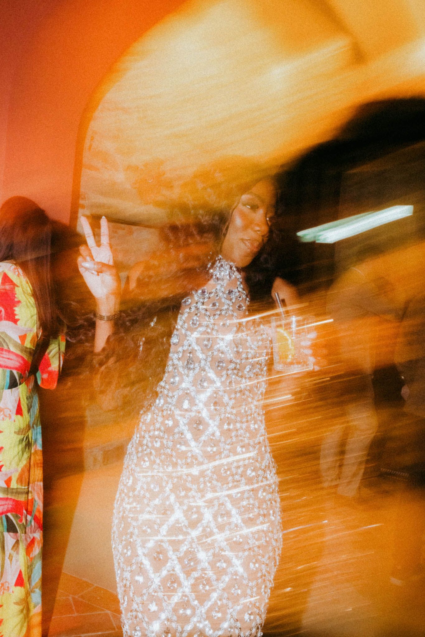Abstract motion blur photographs showing a figure in polka dot dress making peace signs against an orange background.