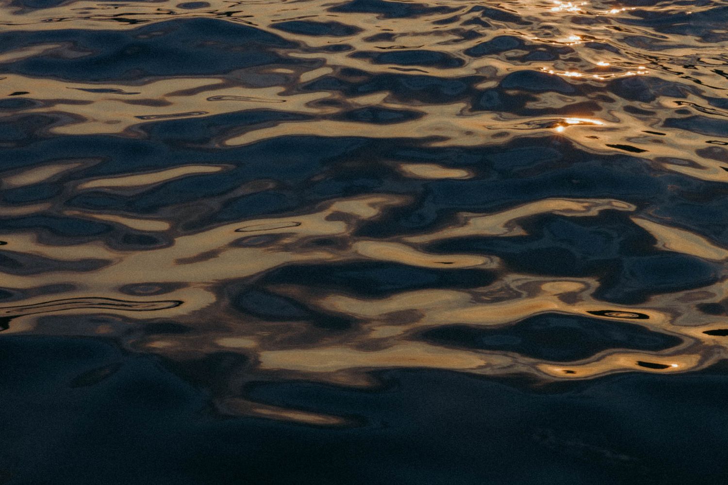 Sunlit ripples on dark ocean water create a mesmerizing pattern of golden reflections at sunset.