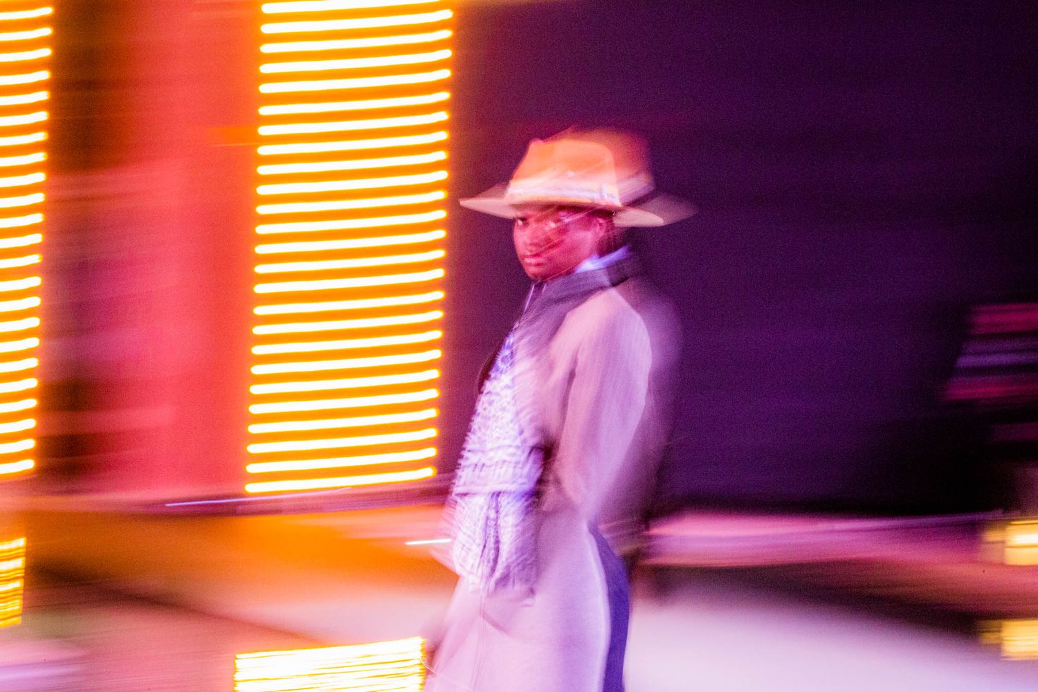 A performer in a cowboy hat stands on stage with colorful orange and purple lighting effects in the background.