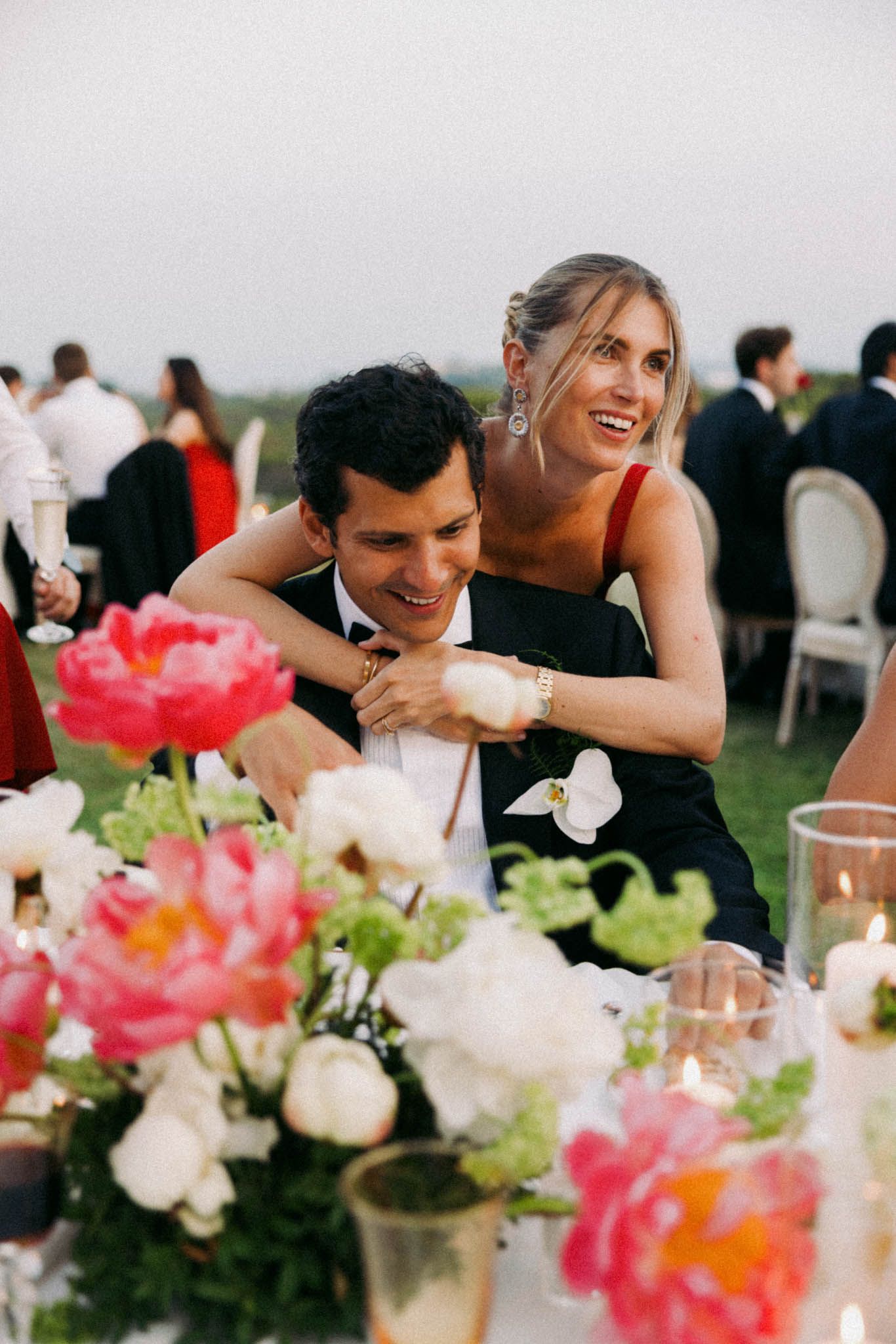 Colorful pink and white floral centerpieces decorate tables at an outdoor wedding reception.