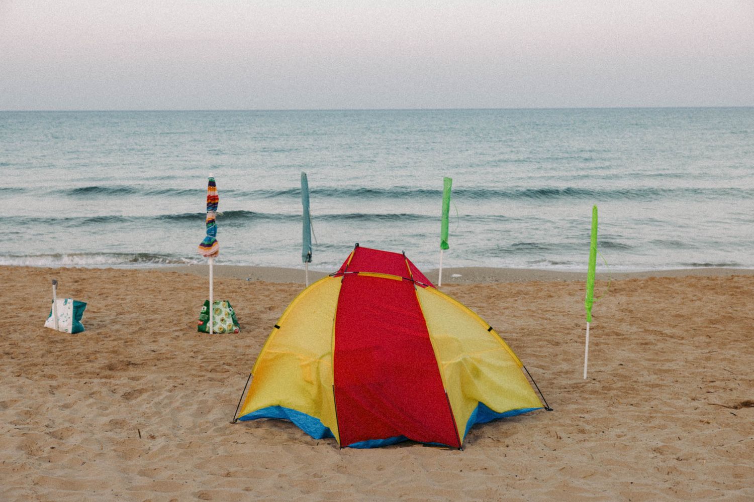 Colorful beach umbrellas and tents line the sandy shore with green poles marking the beach area near the ocean waves.