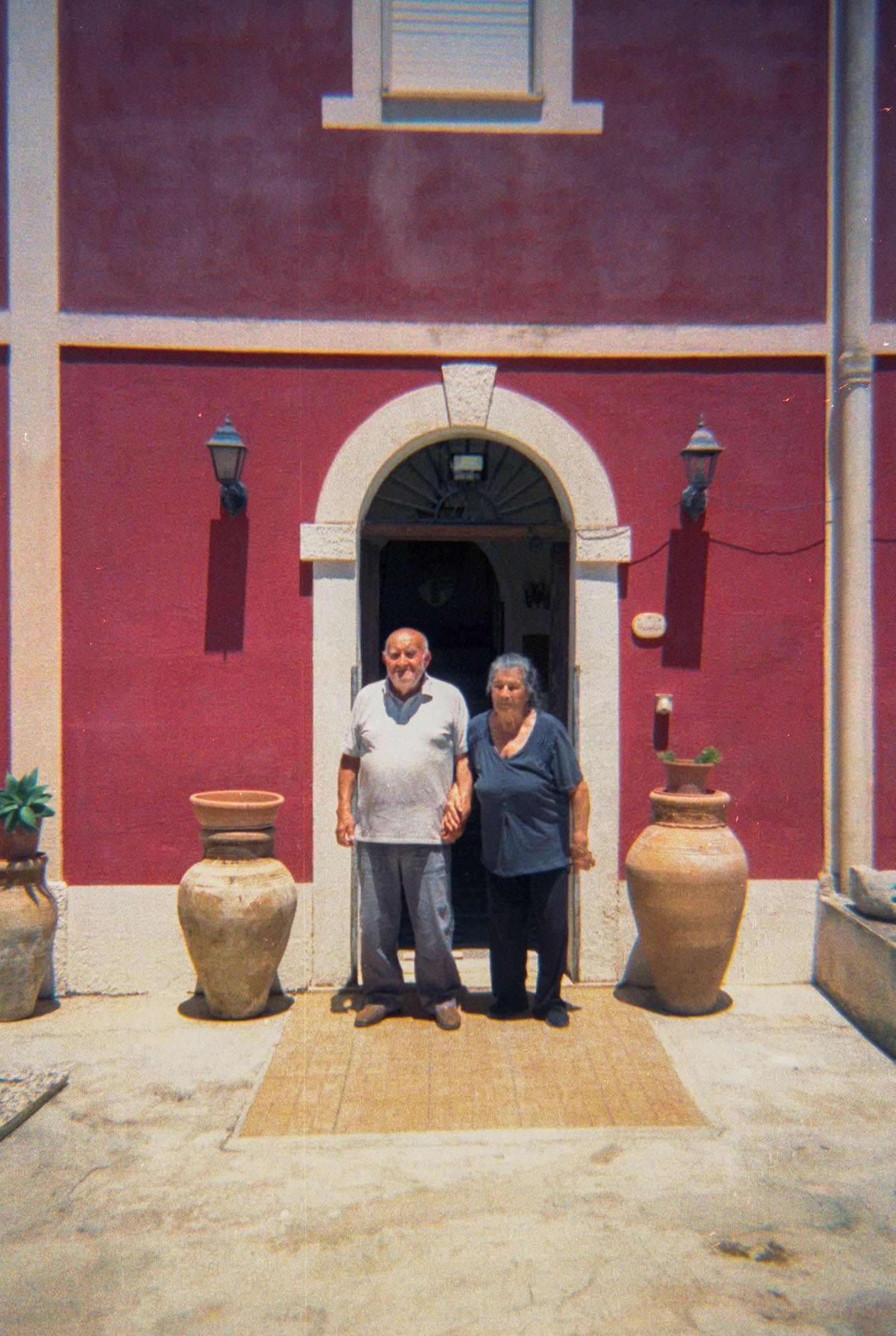 A panoramic view of a rustic red building exterior with large clay pots and arched doorway in Mediterranean style.