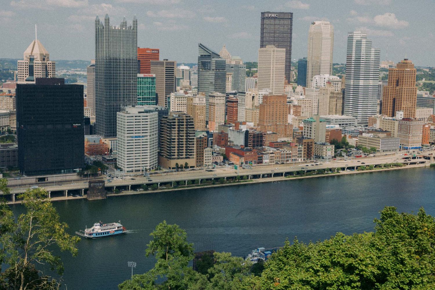 Panoramic view of Manhattan skyline and East River waterfront with tall skyscrapers and boats on a sunny day.