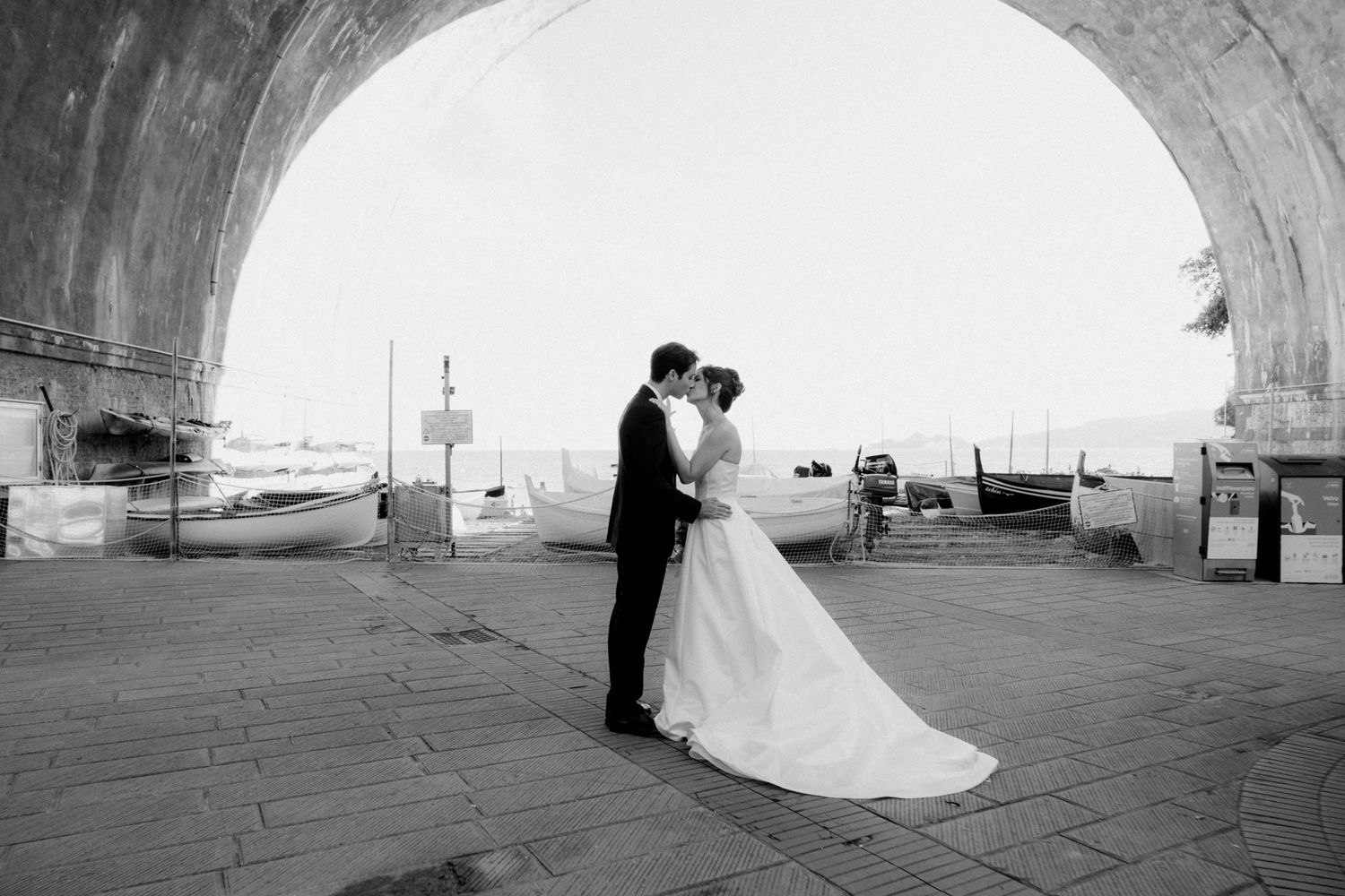 A couple embraces under a stone archway in a black and white wedding photograph.
