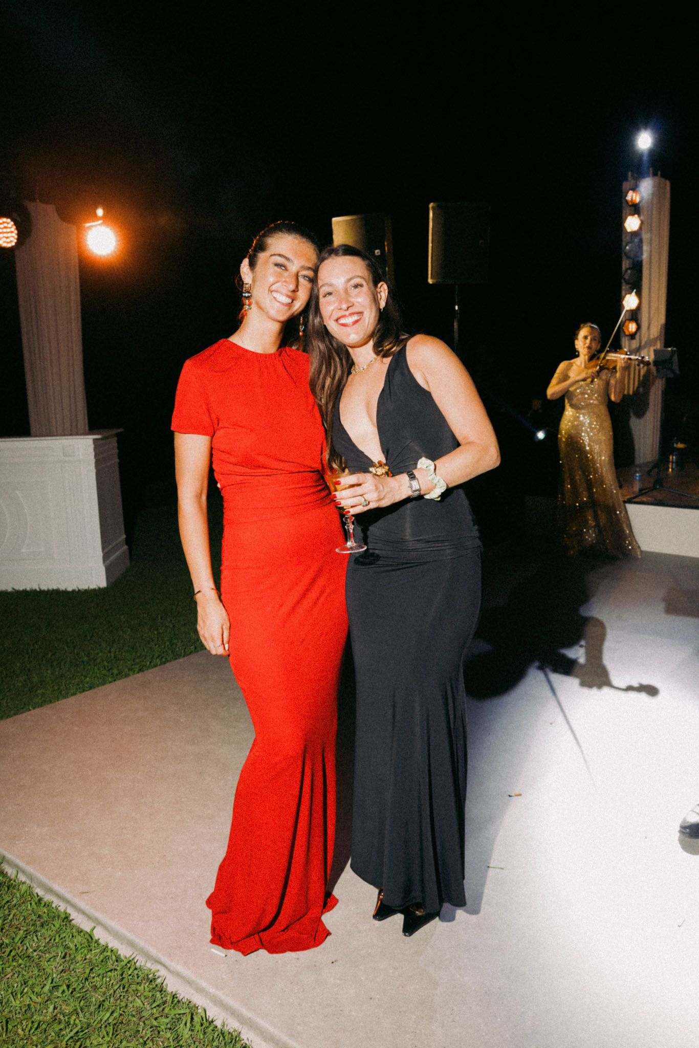 Two people in contrasting red and black dresses pose together at an evening outdoor event.