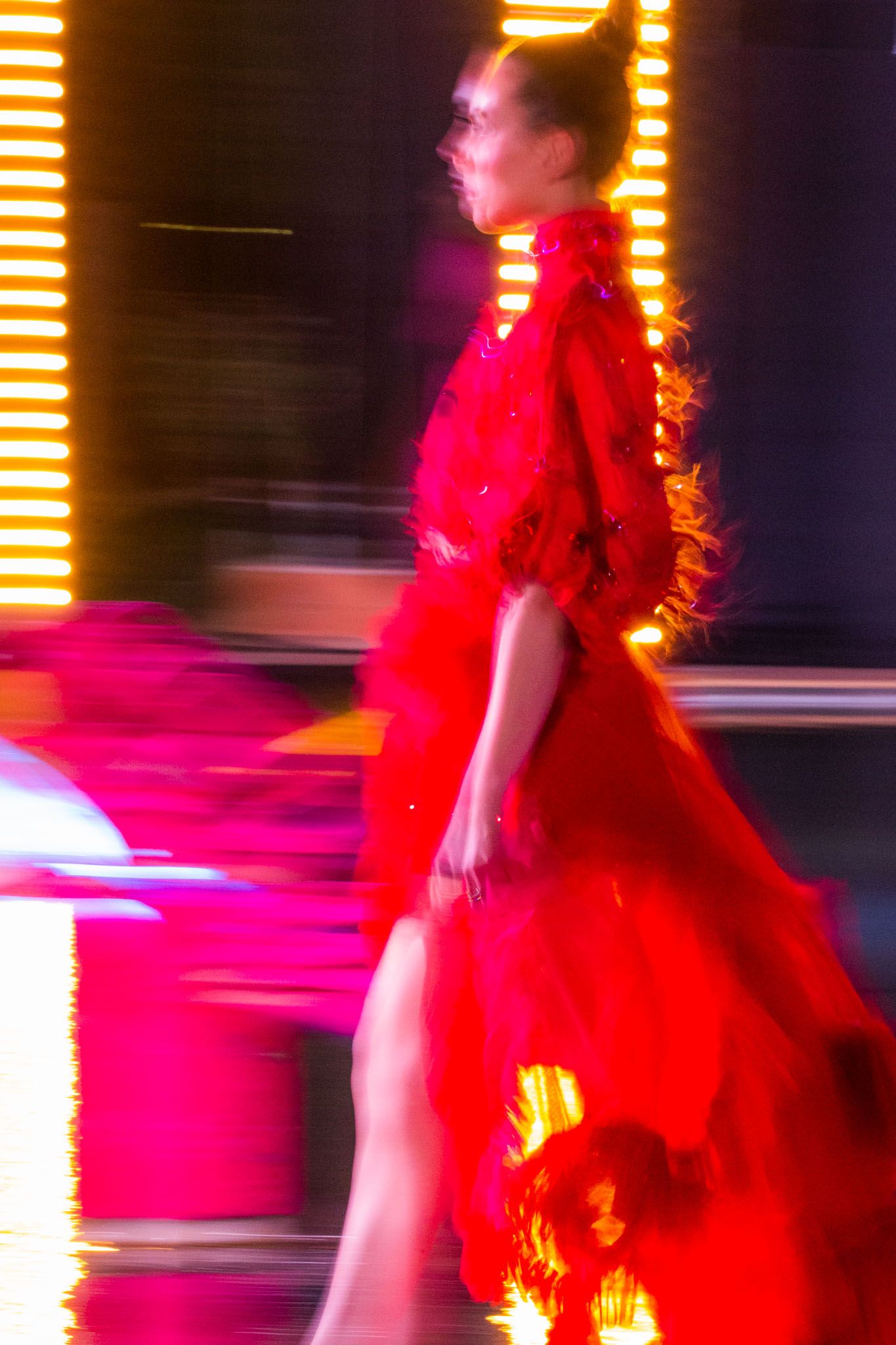Motion-blurred figure in vibrant red dress performing on stage with dramatic orange lighting effects.