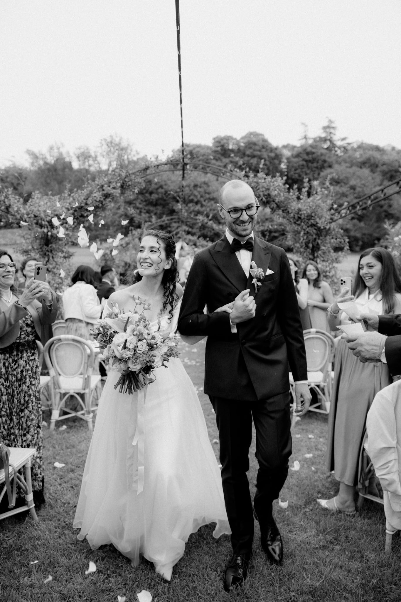 Wedding guests celebrate and mingle during an outdoor garden reception in black and white photography.