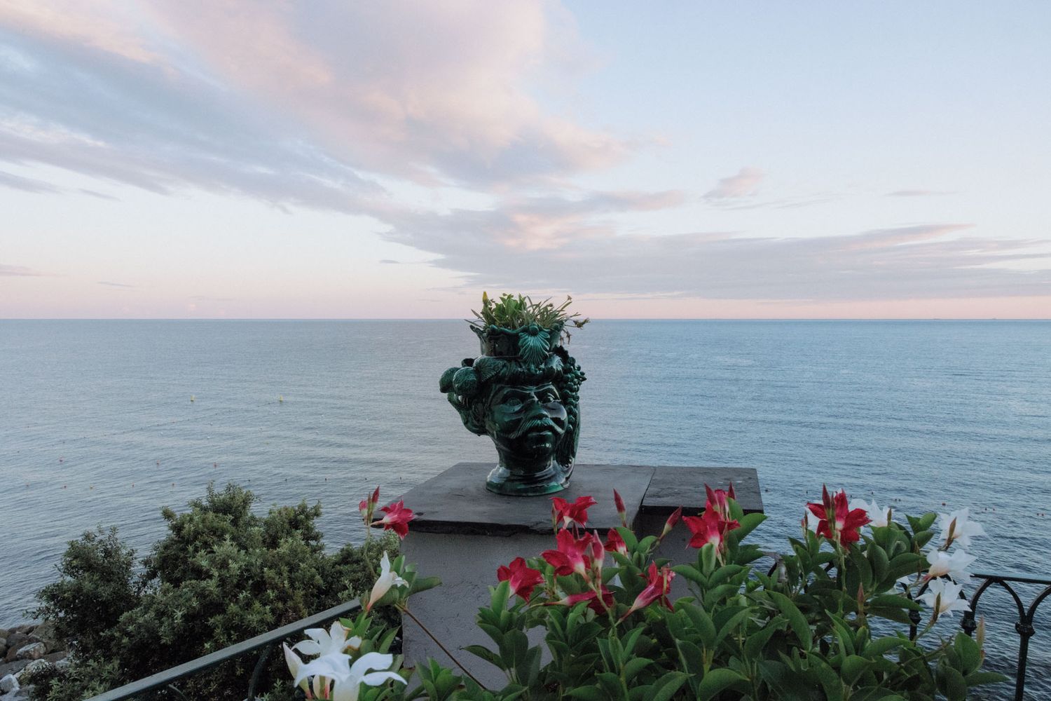 Scenic coastal landscape with red flowers and ocean view at sunset with cloudy skies.