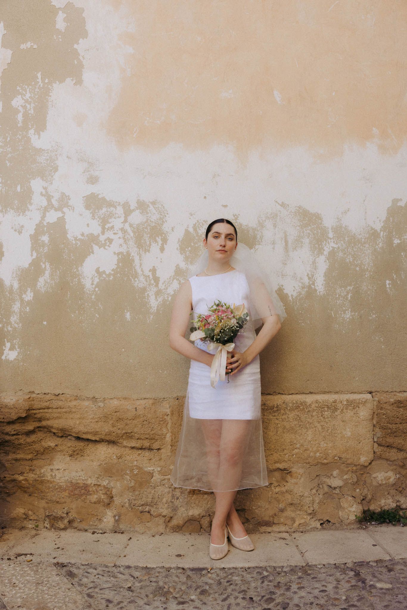 A series of five photos showing someone in white clothing against a weathered beige wall holding a bouquet of flowers.
