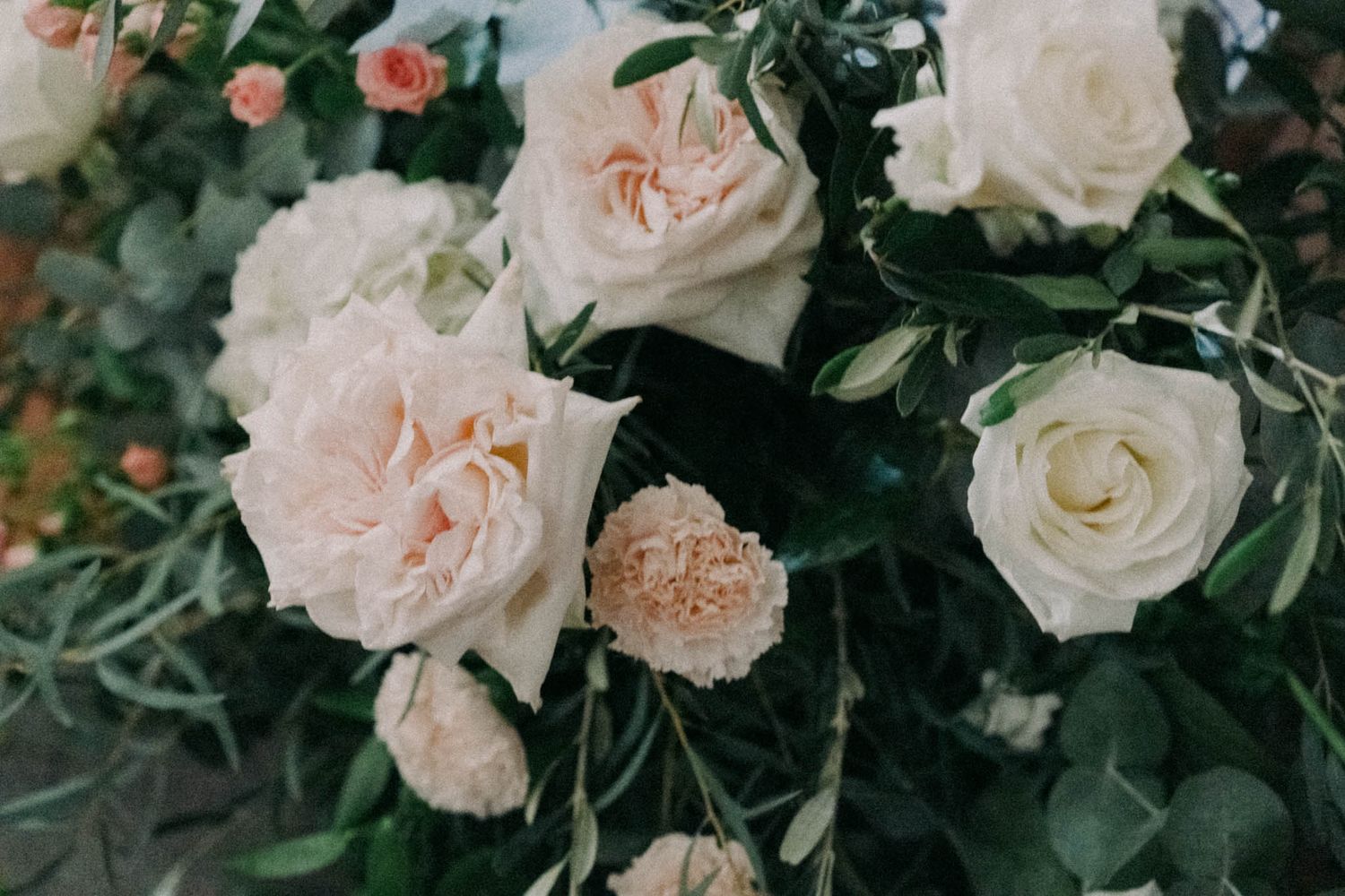 Elegant blush pink and white roses with lush greenery arranged in a romantic garden-style floral display.