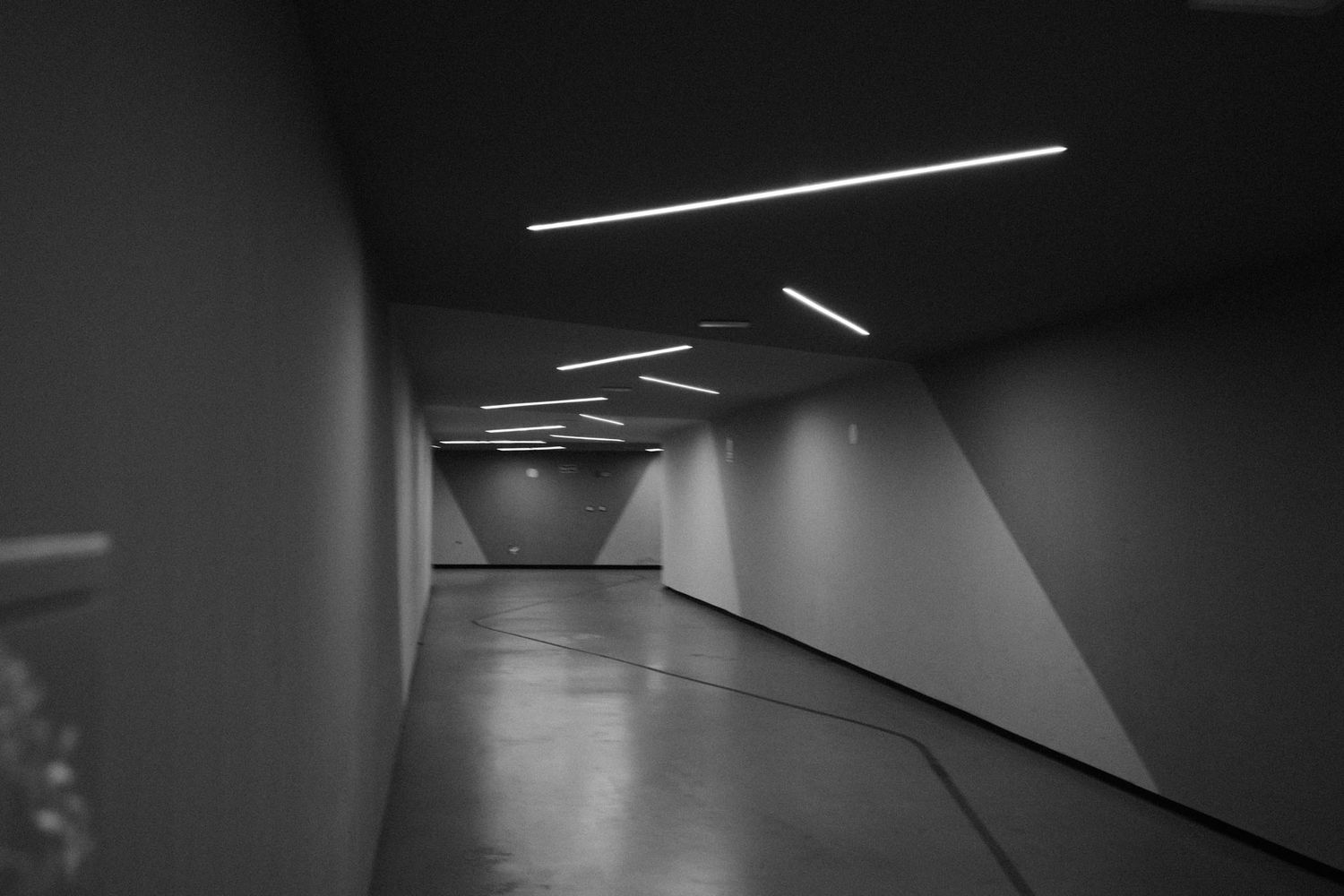 A minimalist hallway with fluorescent lighting and angular walls creates a stark monochromatic perspective.