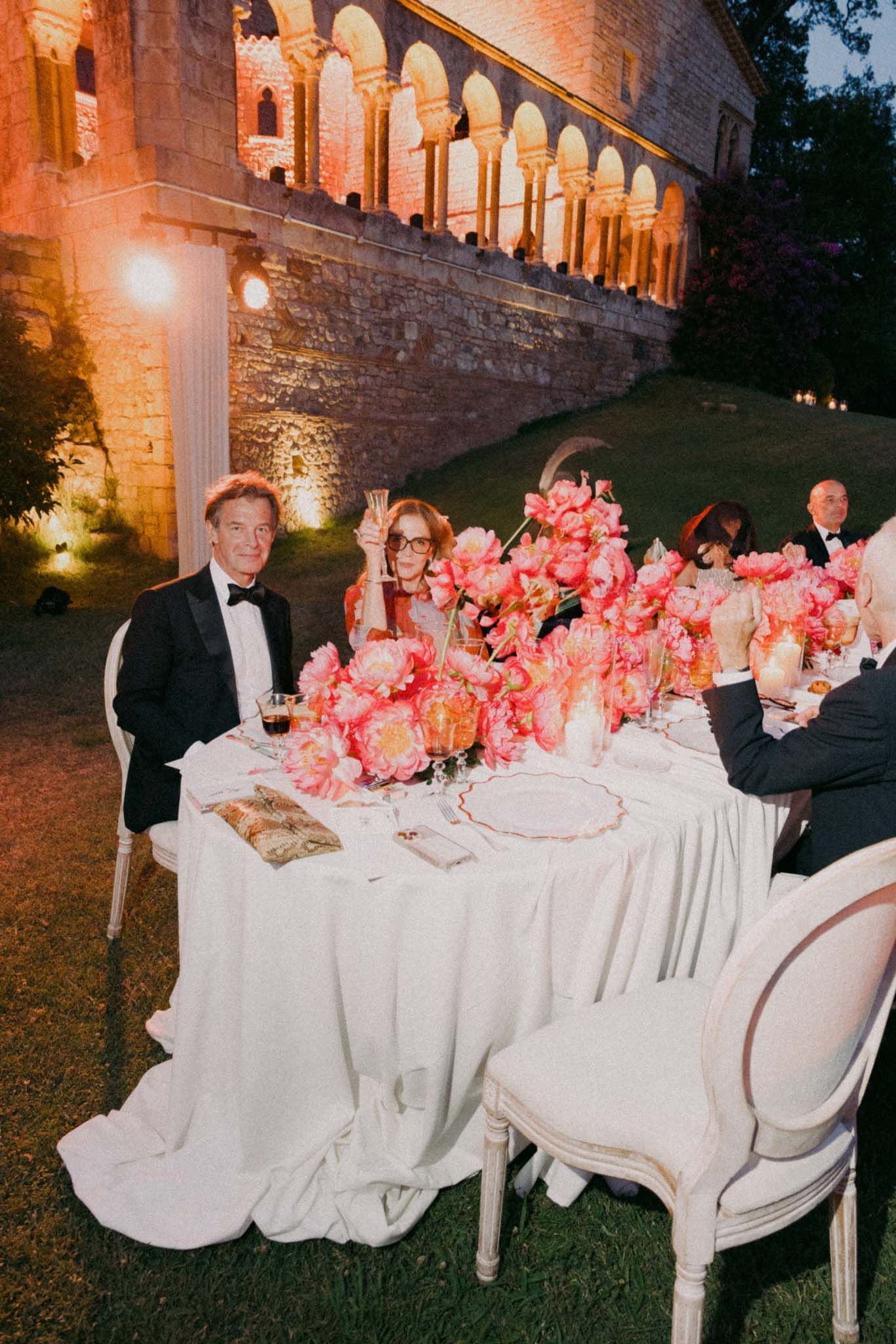 Elegant wedding reception dinner table with pink floral centerpieces and glowing candlelight at a historic stone venue.
