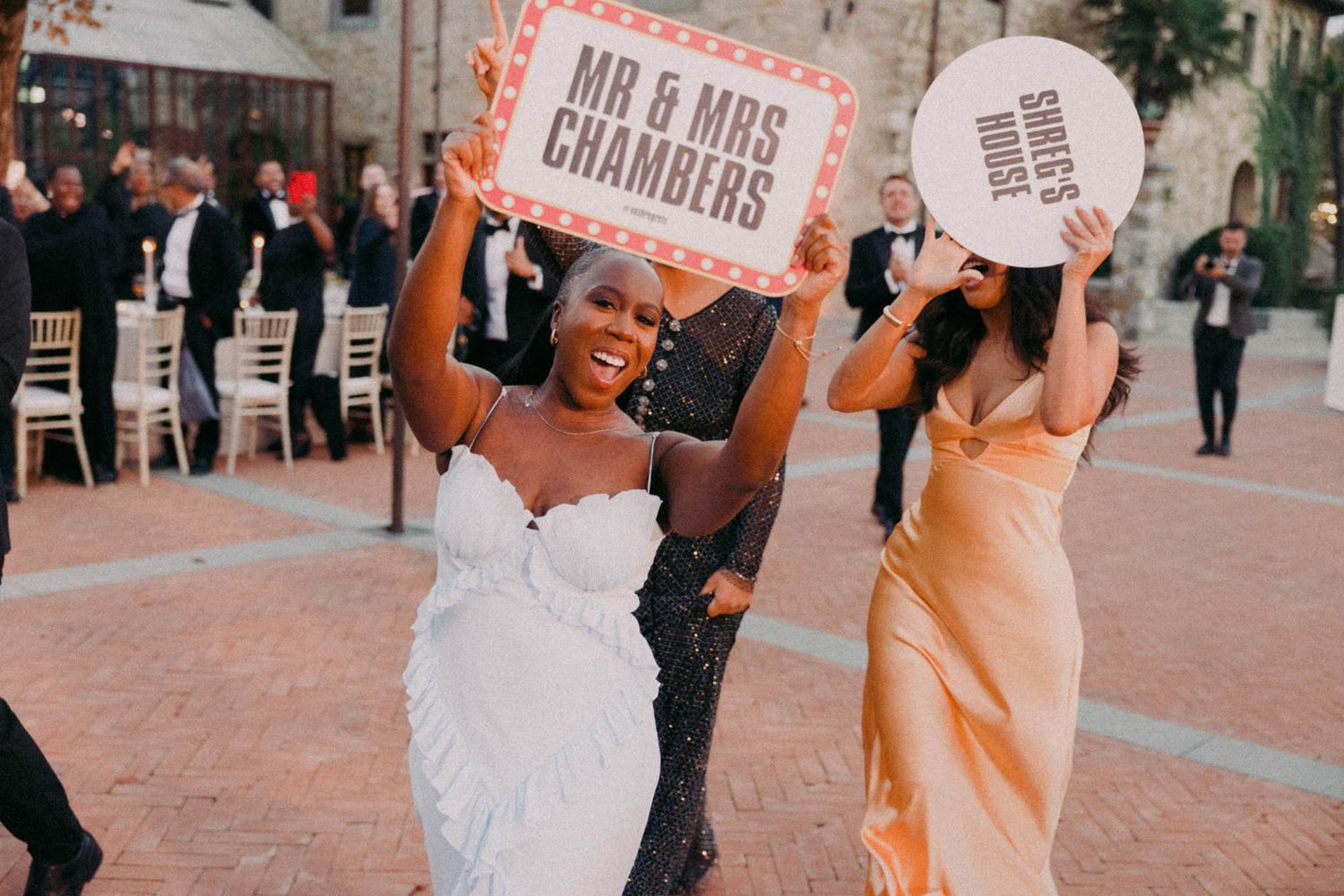 A joyful wedding celebration with people dancing and holding signs in an outdoor urban setting.