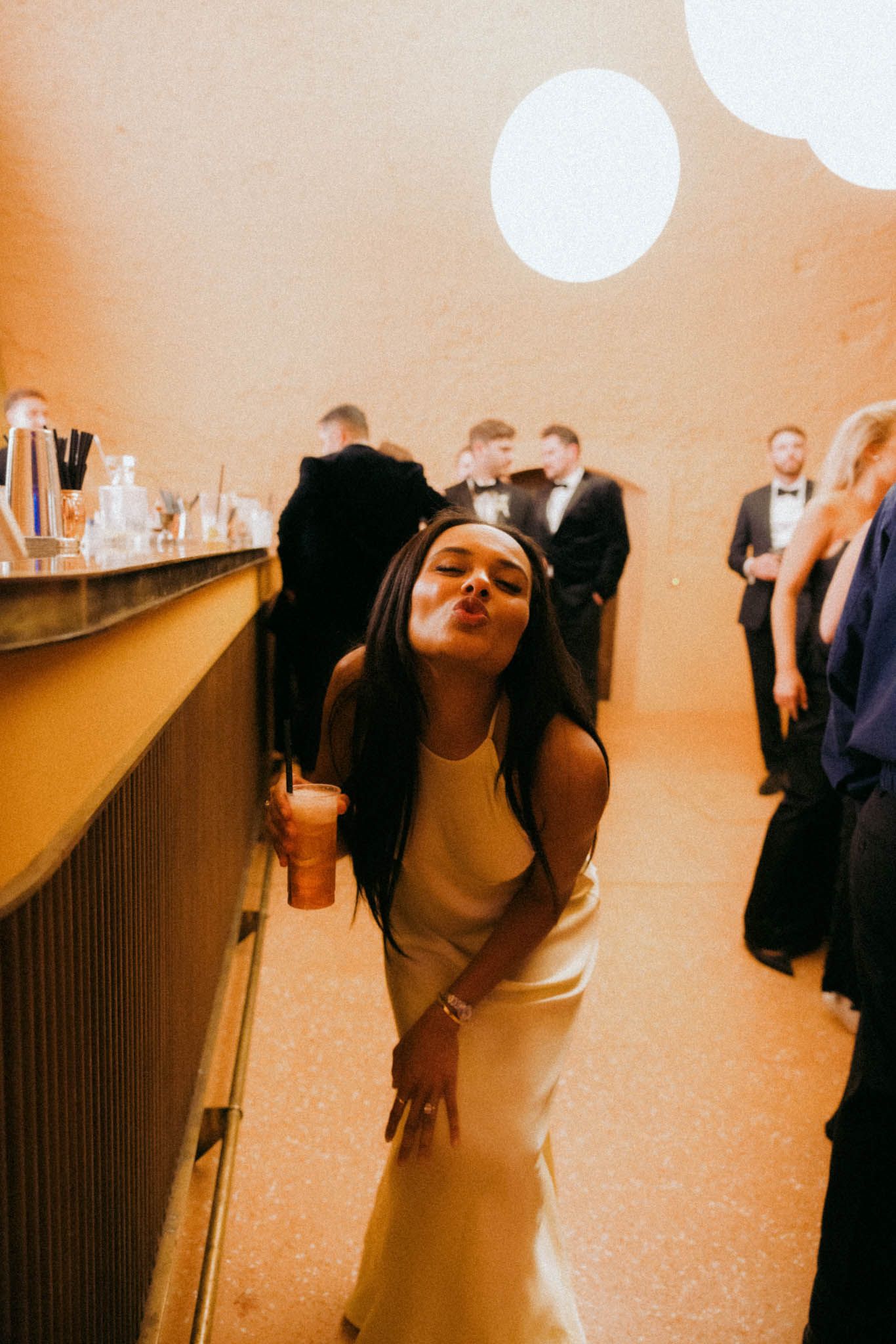 People dancing and celebrating at a party with bright spotlights and warm ambient lighting.