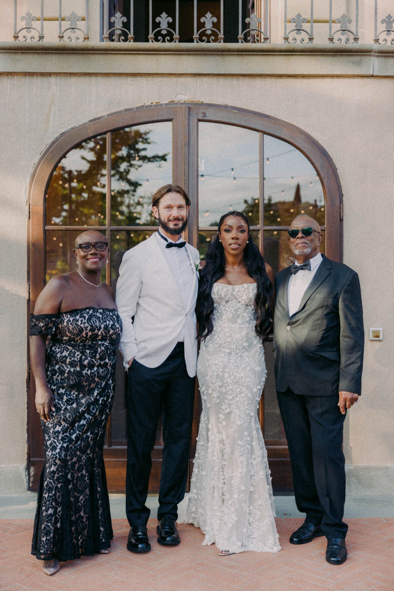 Four people in formal attire pose together in front of an arched doorway at an elegant venue.