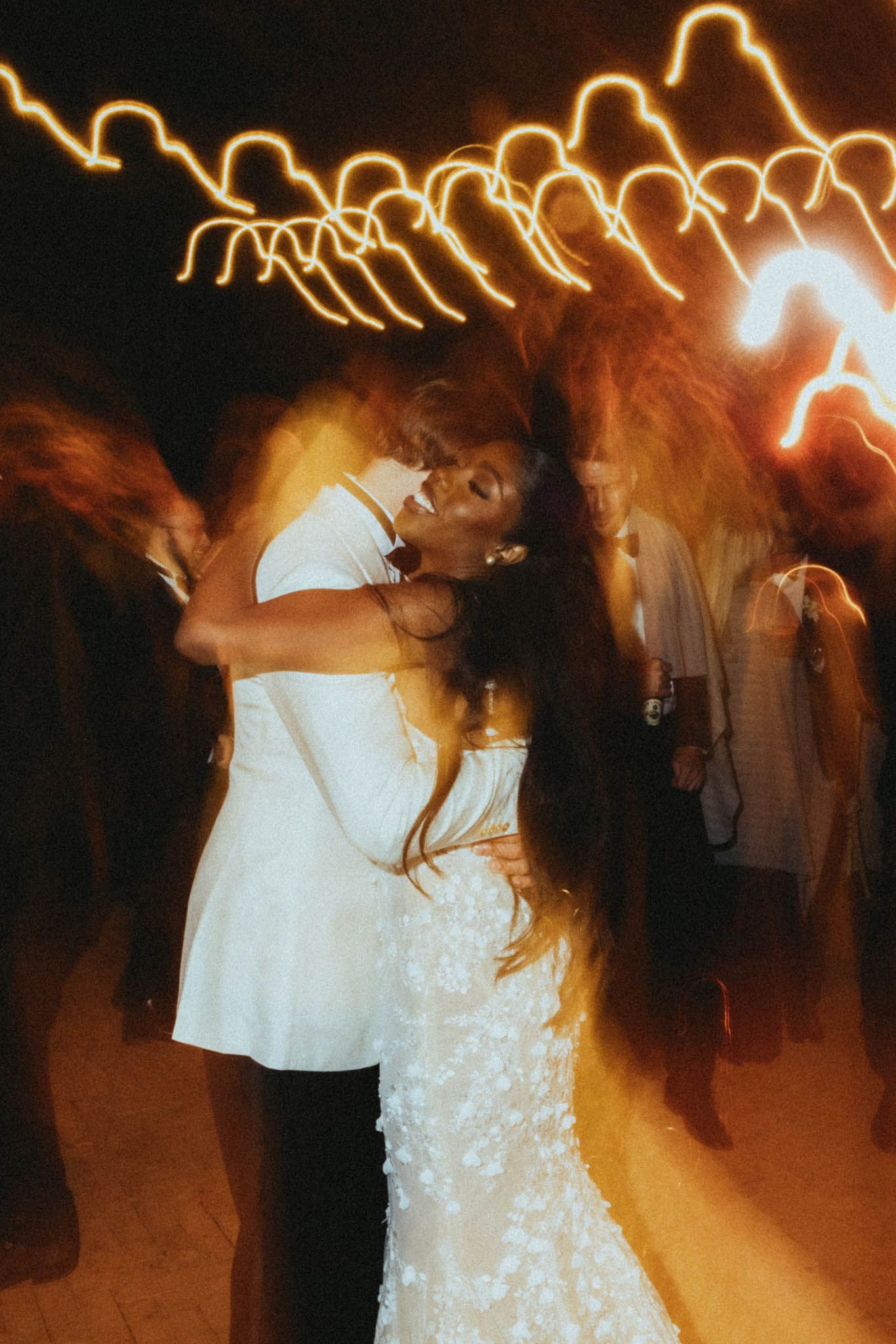A couple shares a romantic dance at a wedding reception with blurred motion and warm lighting creating a dreamy atmosphere.