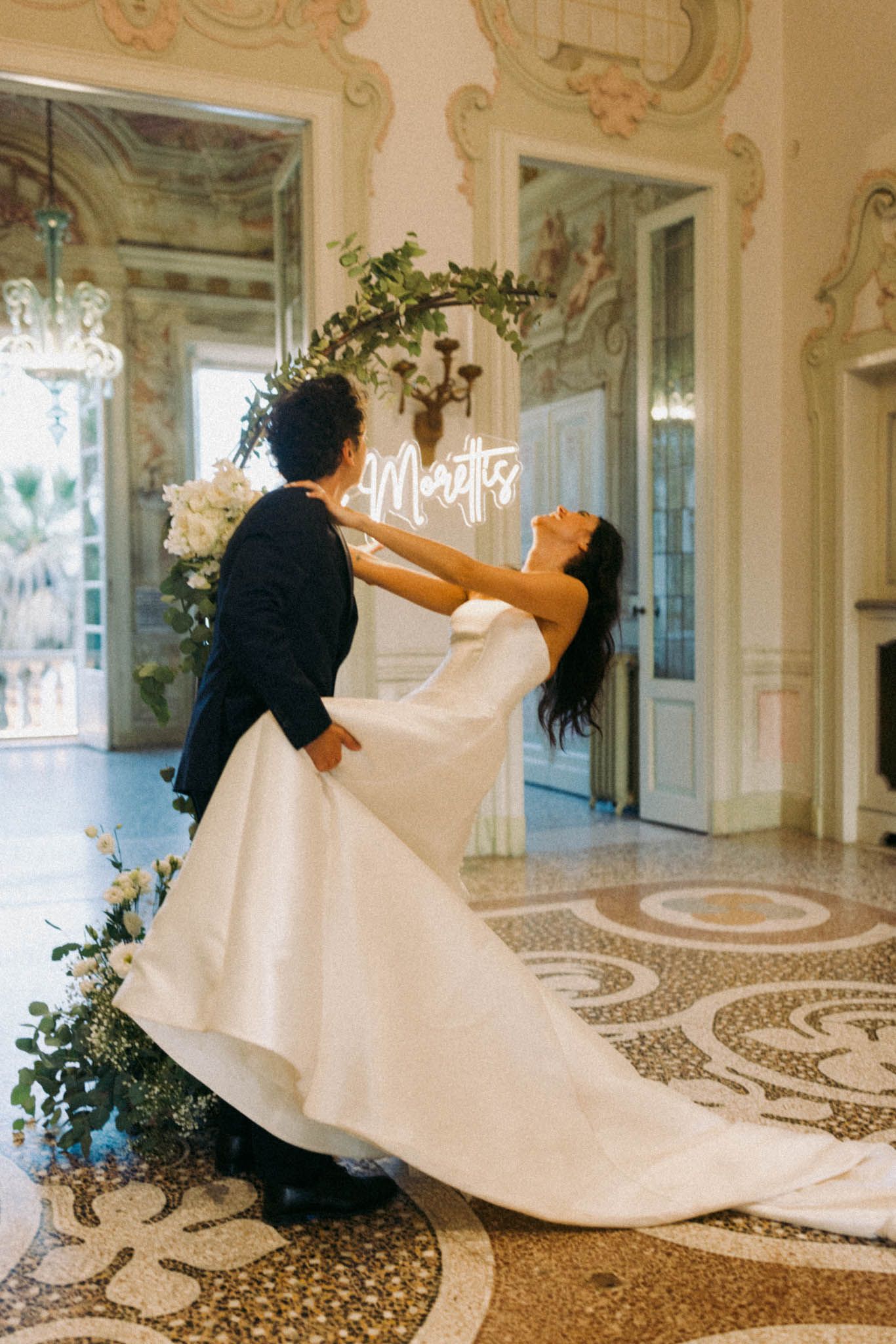 Wedding couple dancing and twirling in an elegant ballroom with ornate marble floors and columns.