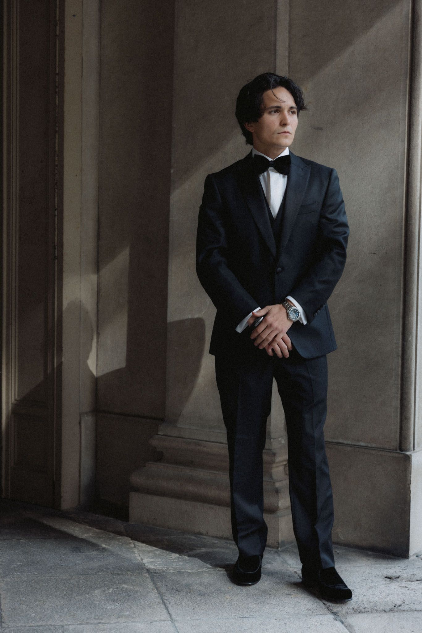 A person in a dark business suit crouches in a dimly lit corridor with concrete walls and floor.