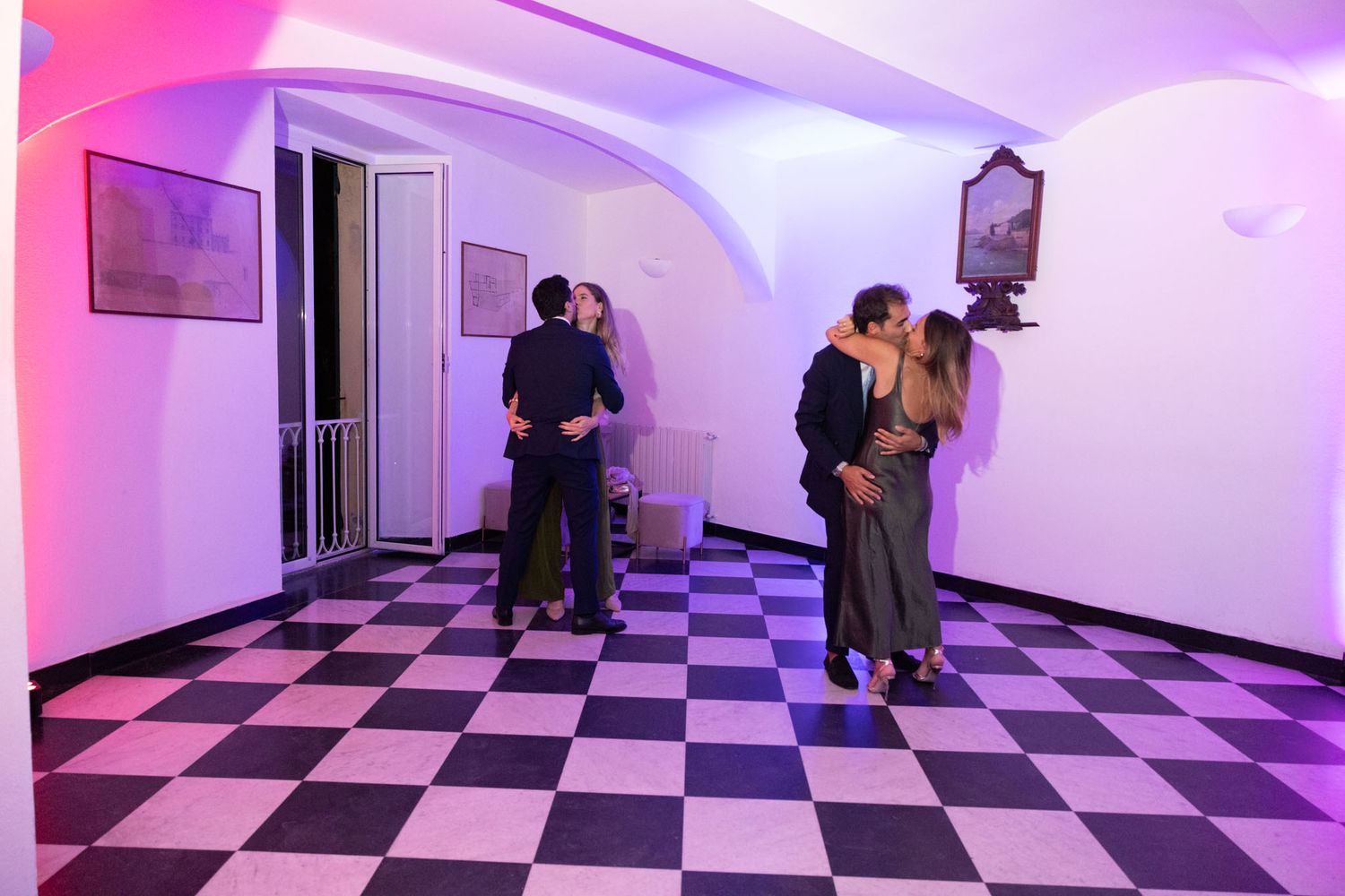 Pink and purple lit hallway with black and white checkered floor shows multiple doorways and curved walls.