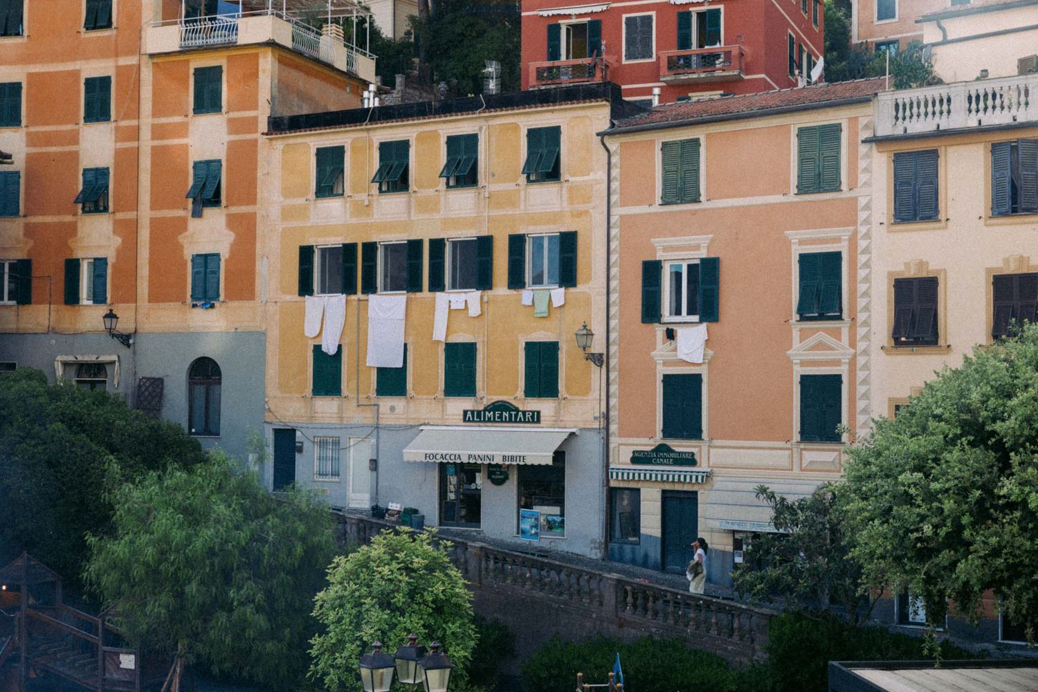 Colorful traditional Italian buildings with terracotta roofs and green trees line a street in Portofino, Italy.