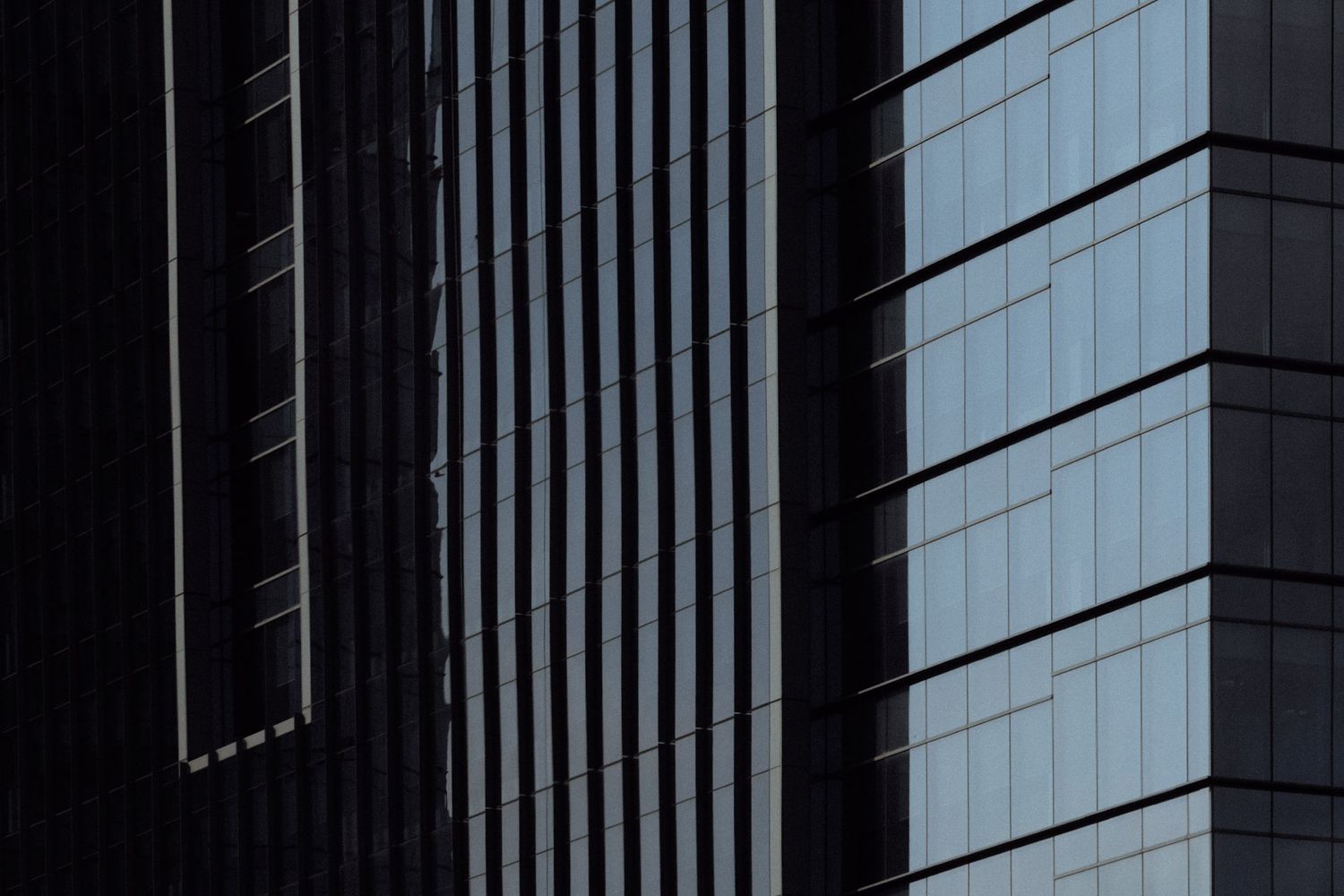 Modern glass office building facade with reflective windows and geometric patterns against dark background.