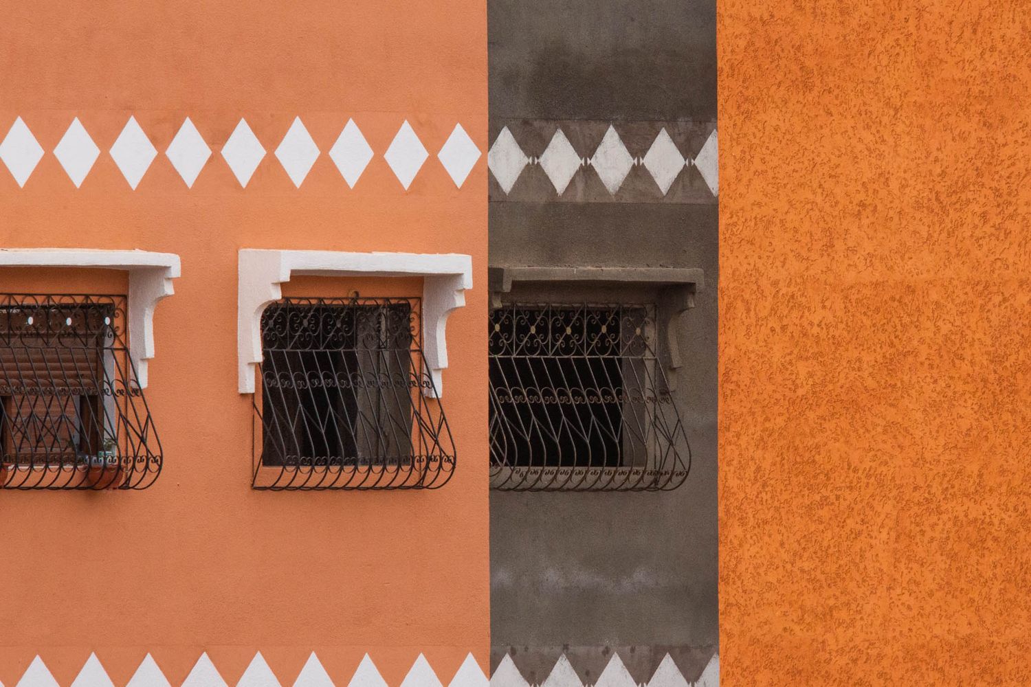 A bright orange stucco wall with ornate metal window bars and white diamond pattern details creates a striking architectural facade.