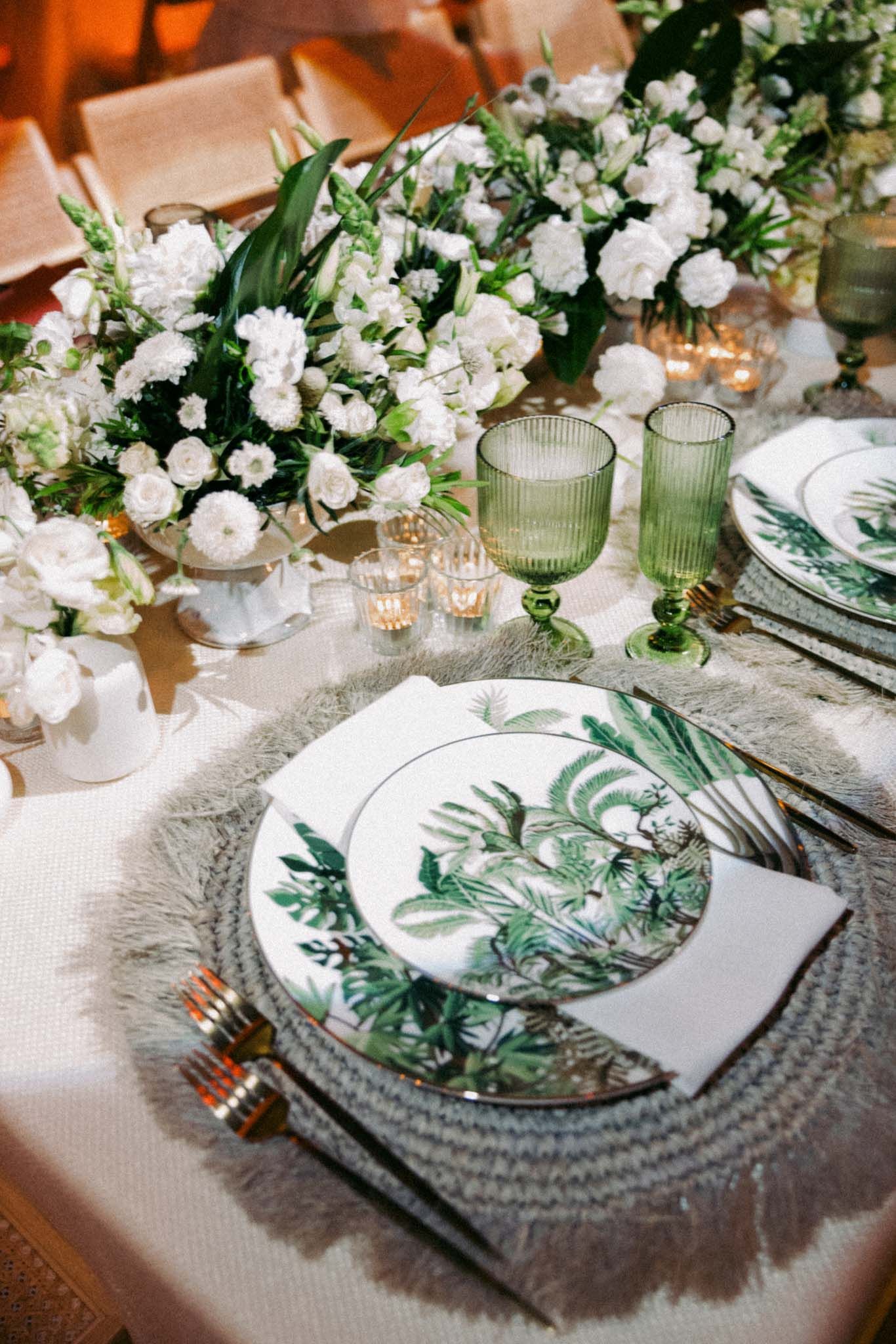 Elegant table setting with green botanical plates, white flowers, and gray placemats for a formal dinner.